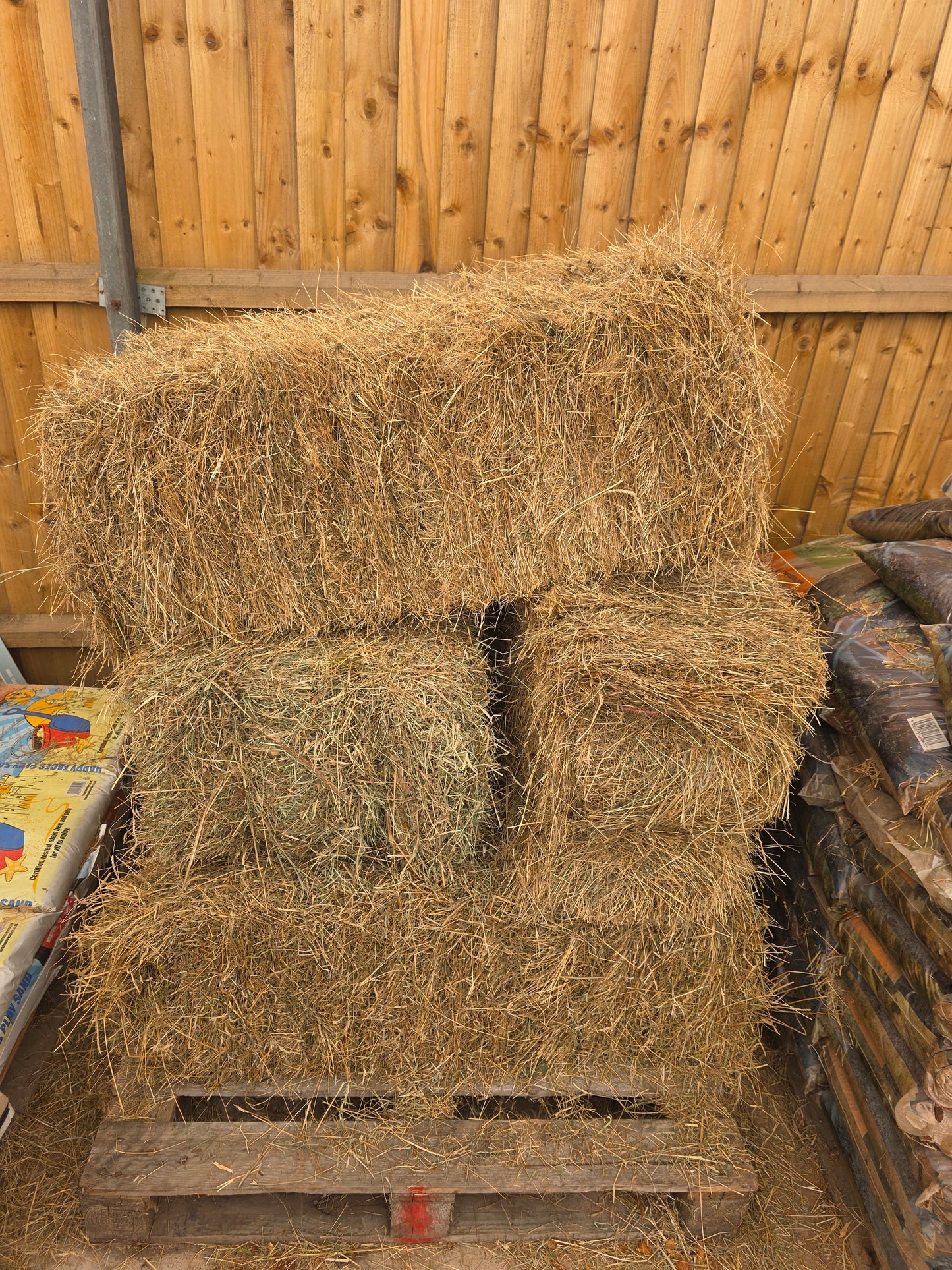 Hay bales on a wooden pallet with a wooden wall in the background