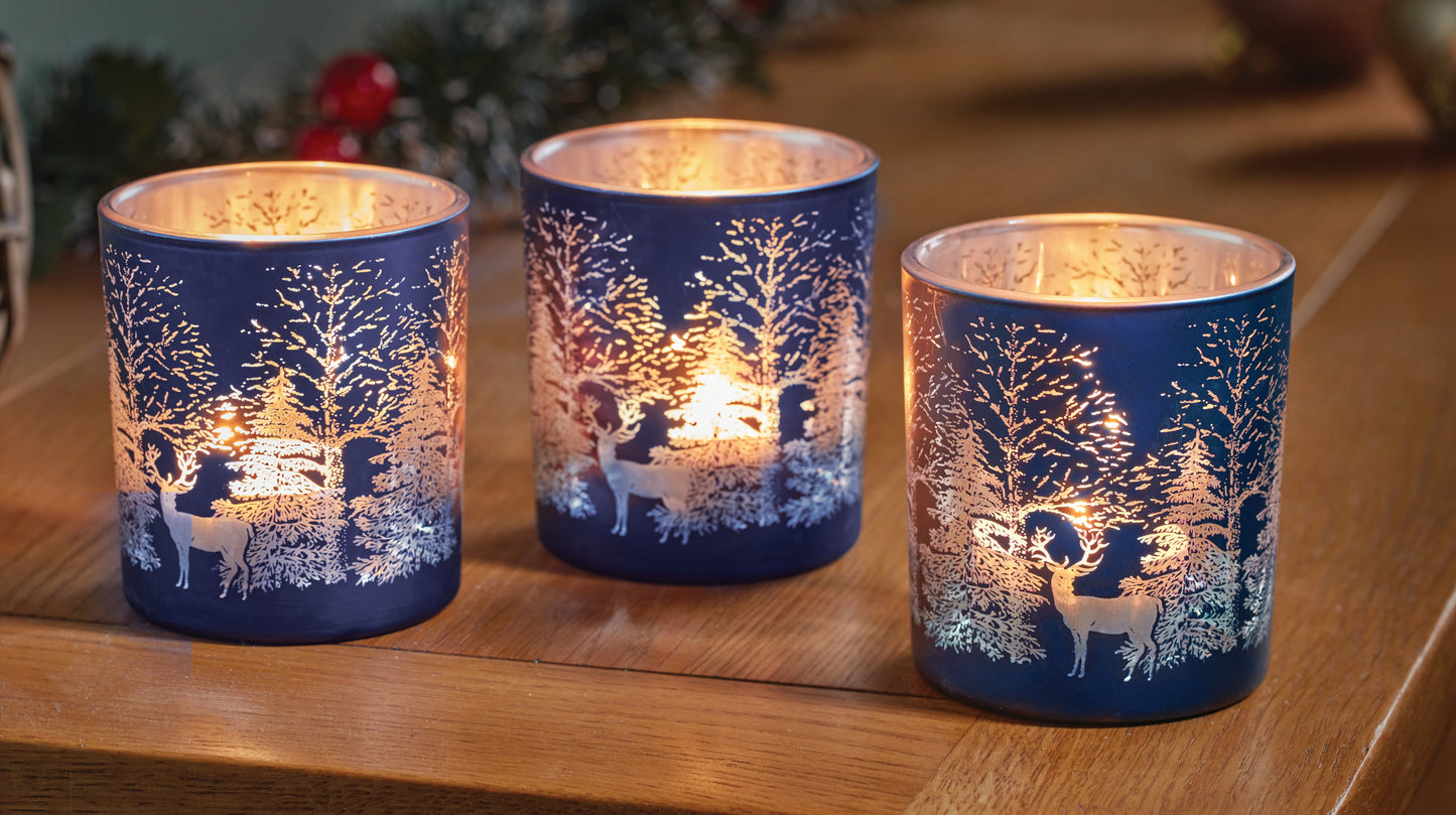 Three blue candle holders with winter scene designs on a wooden surface.