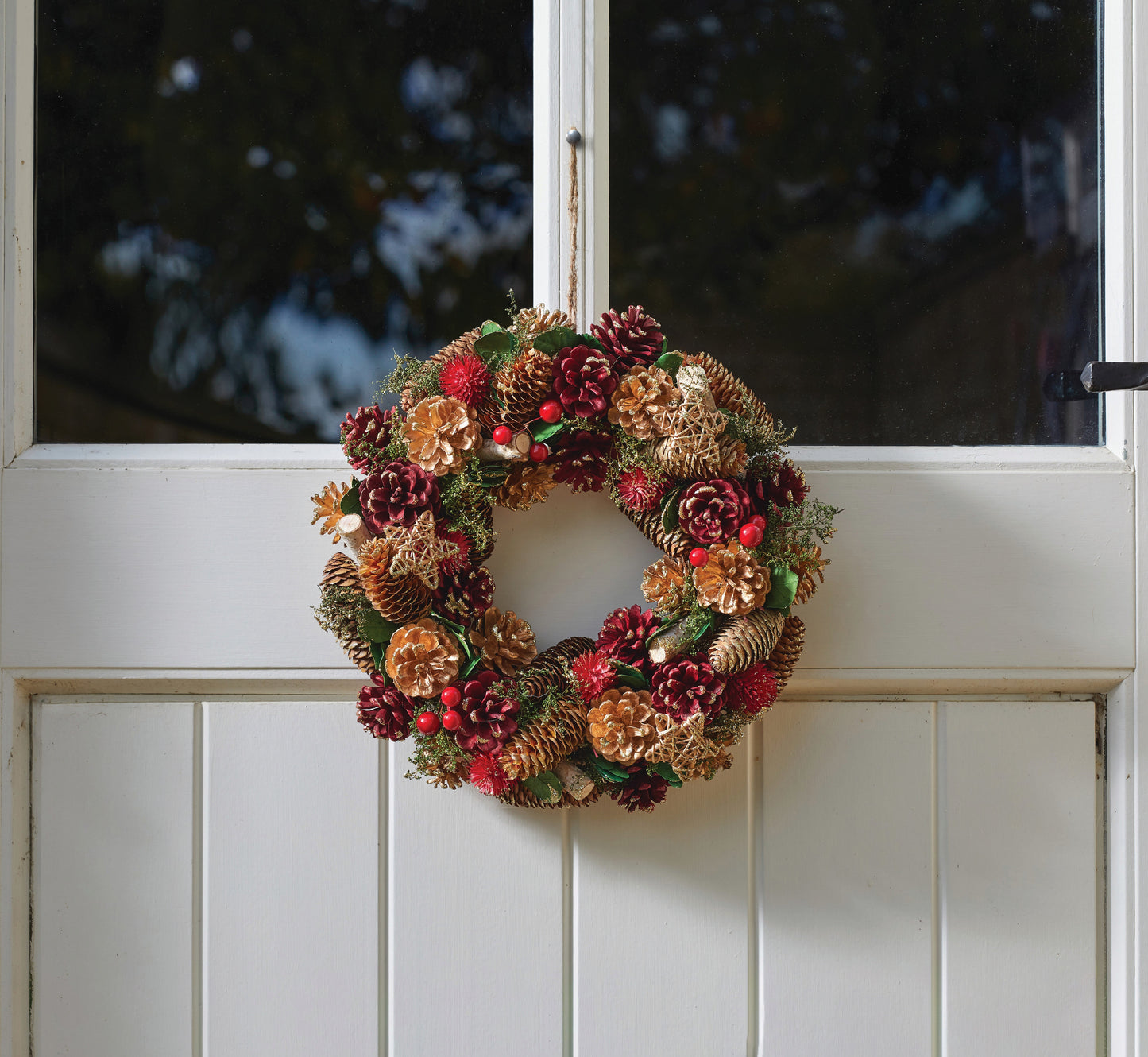 Decorative wreath with pinecones and flowers on a white door