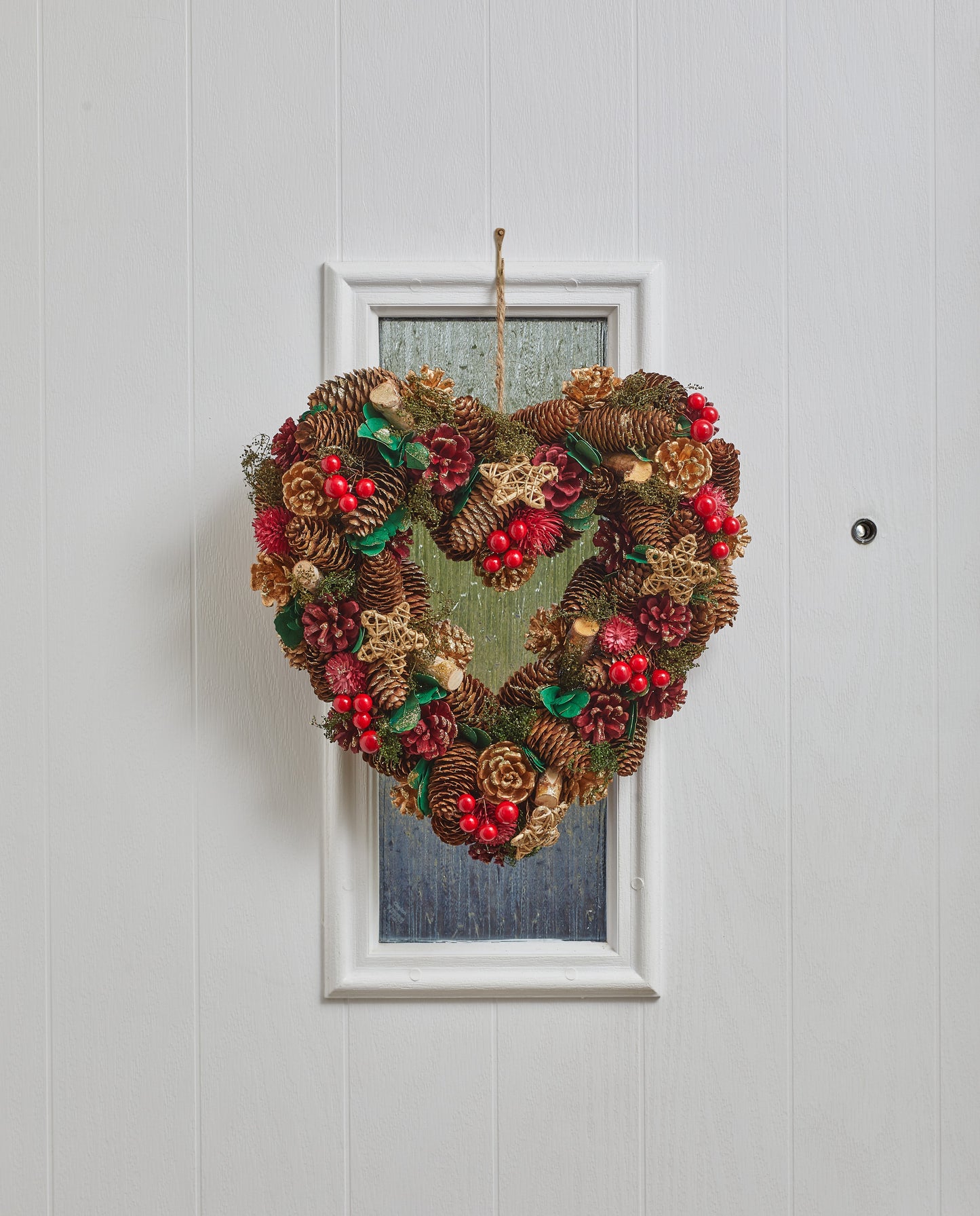 Heart-shaped Christmas wreath with pinecones and berries on a white door.