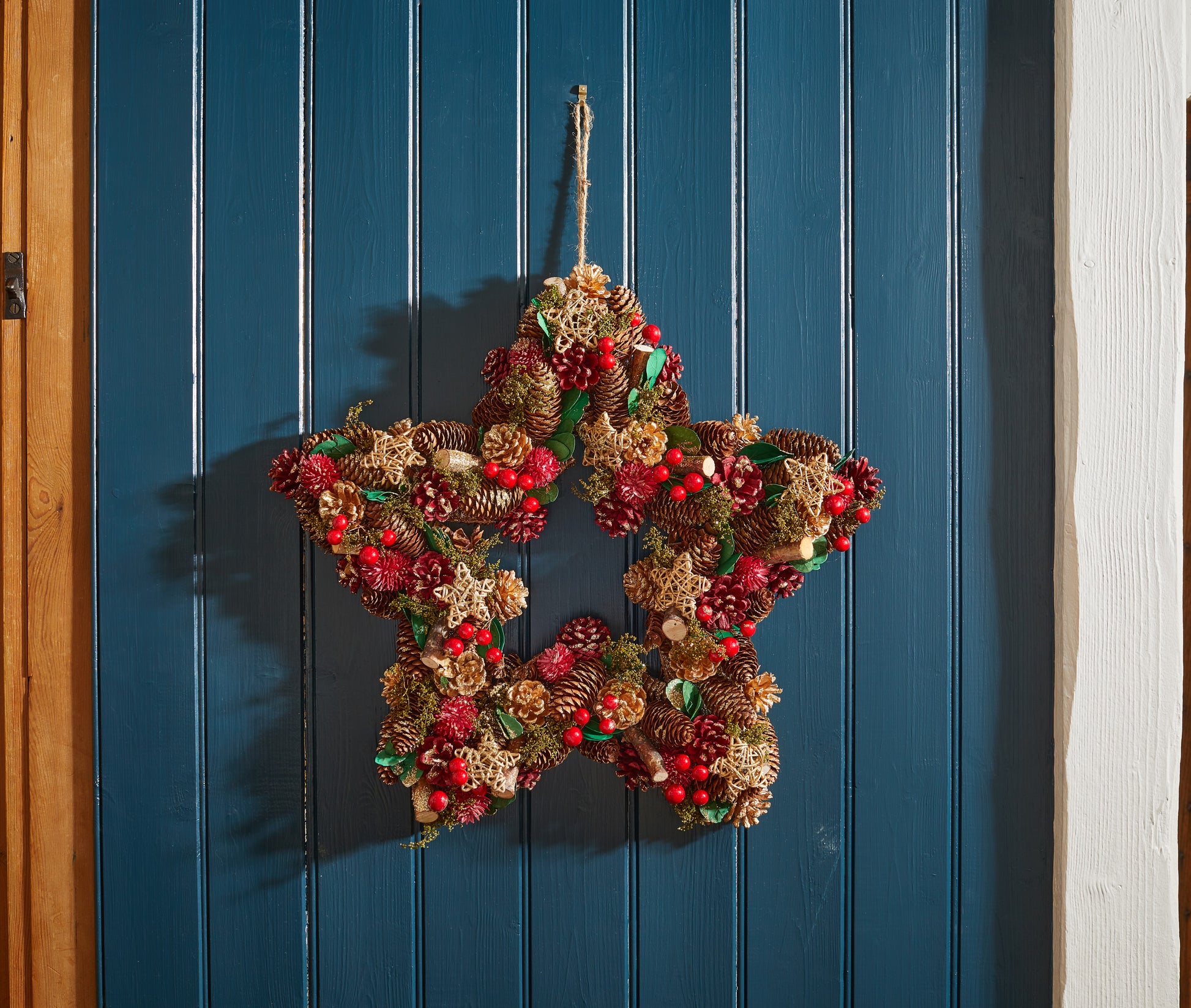 Decorative star-shaped wreath with pinecones and berries hanging on a blue wooden door.