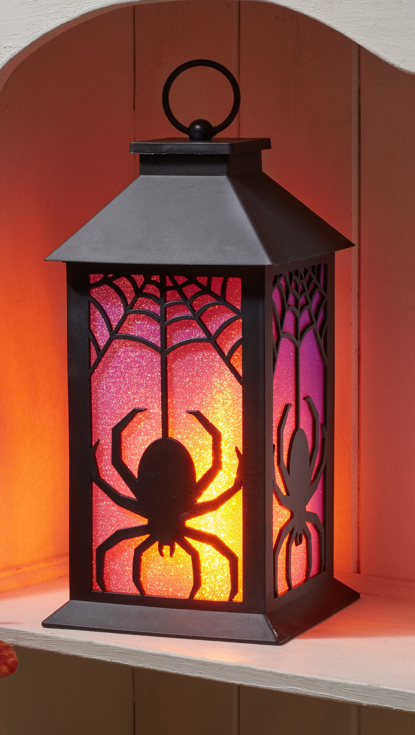 Halloween-themed lantern with spider design on a wooden shelf.
