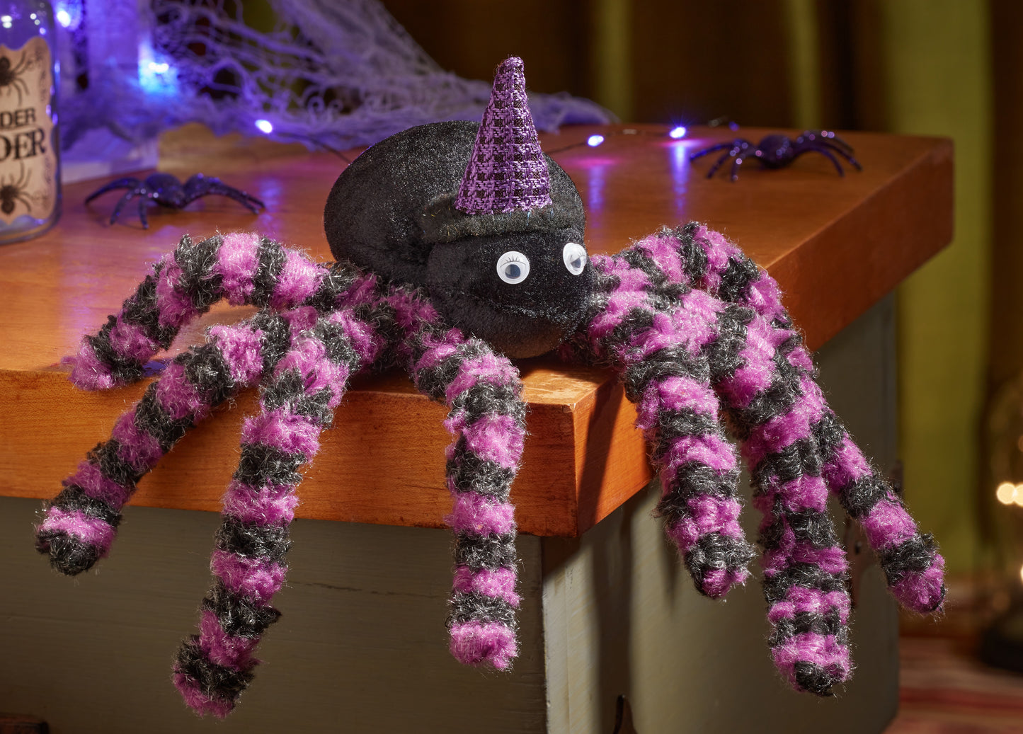 Spooky toy spider with a witch hat on a wooden surface, surrounded by Halloween decorations.