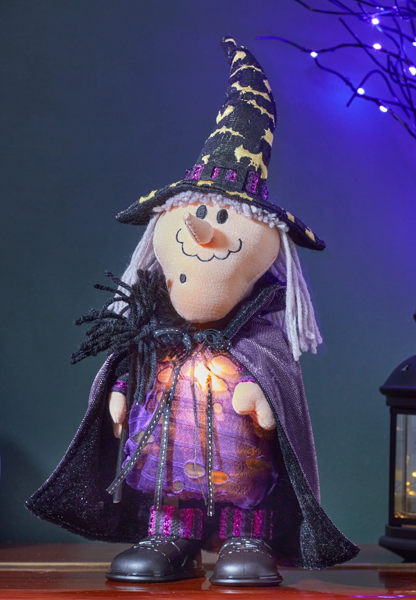 Decorative witch figurine with a purple cape and black hat on a dark background.
