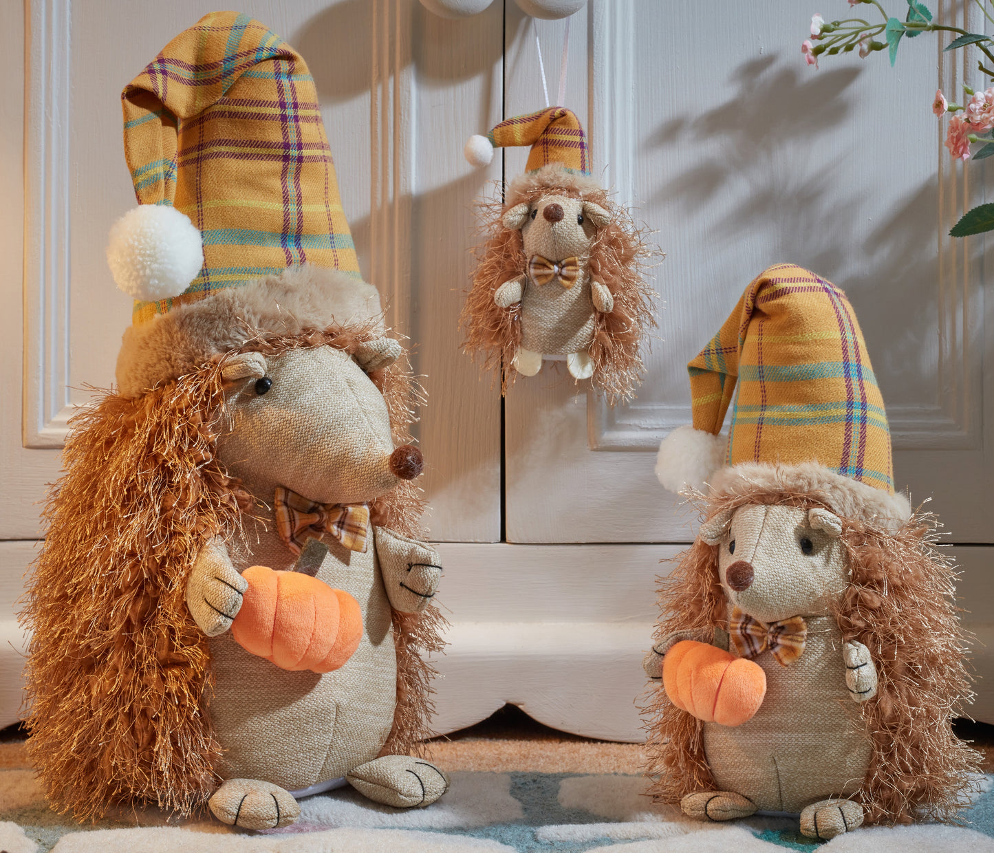 Three plush hedgehogs with plaid hats and pumpkin patches on a wooden floor.