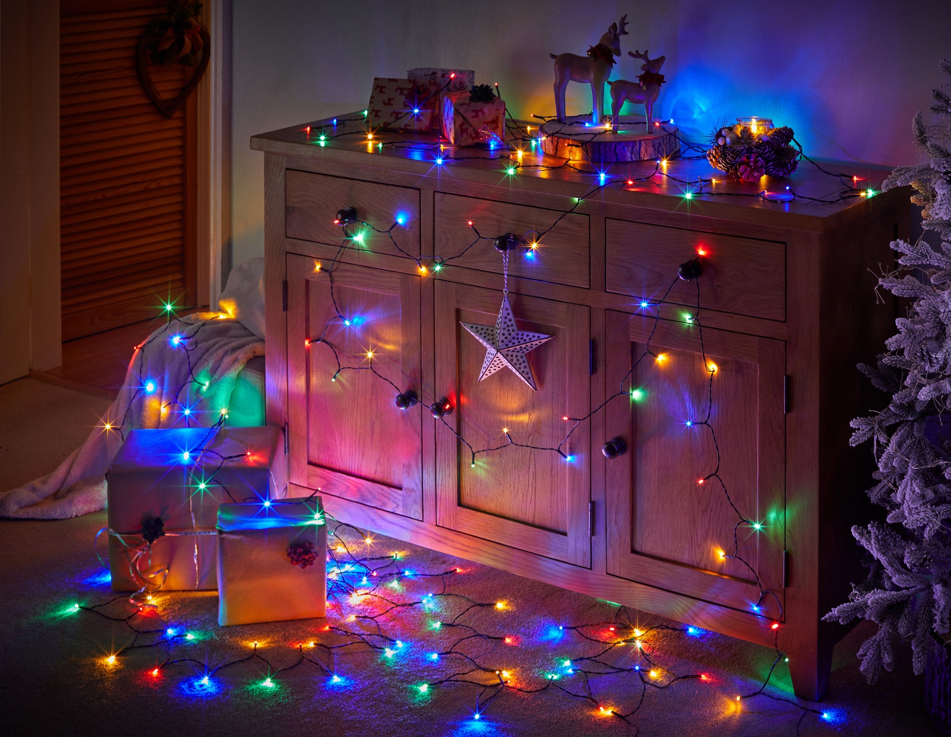 Wooden cabinet decorated with colorful string lights and Christmas decorations in a cozy room.