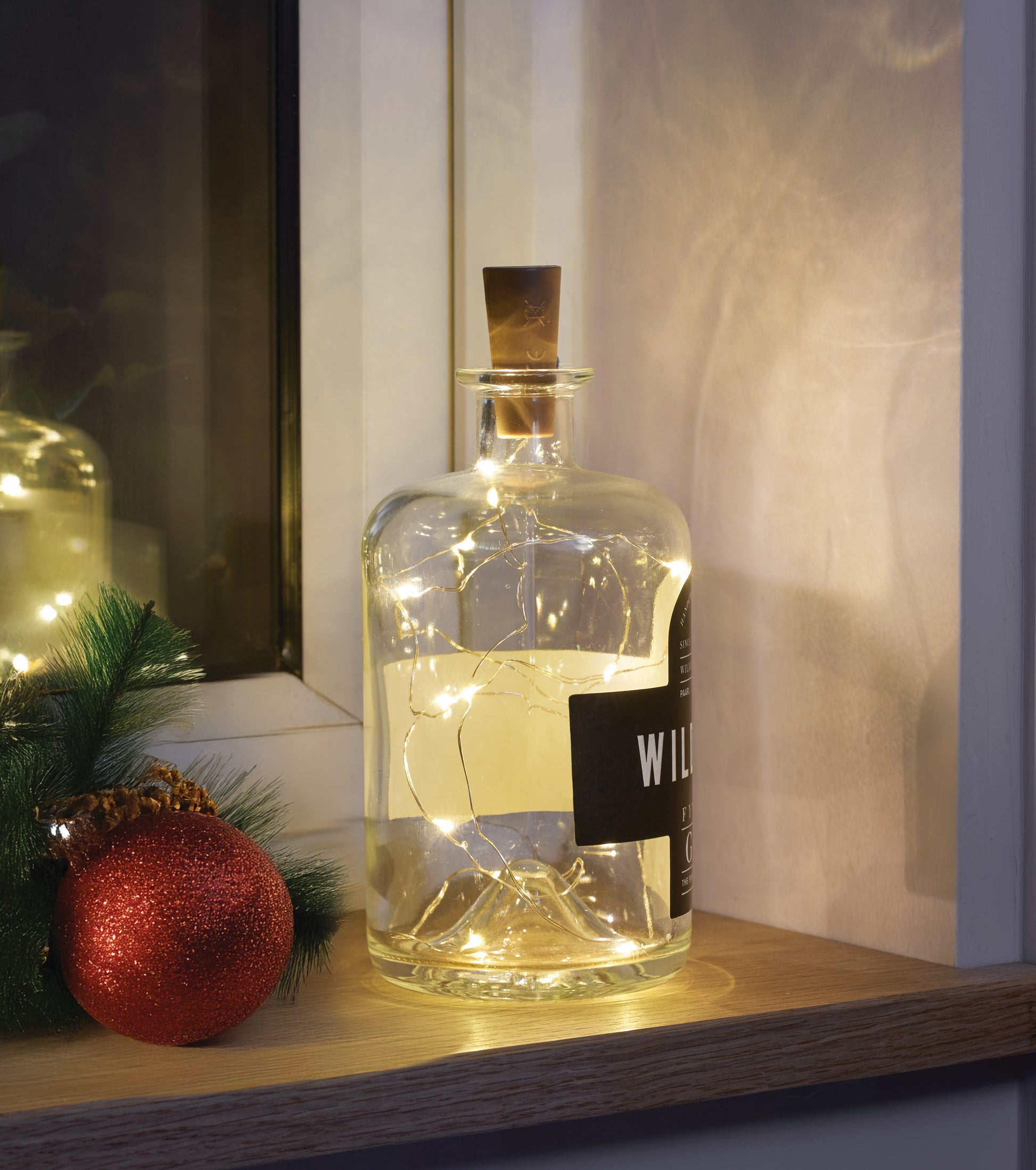 Decorative bottle with string lights on a shelf with festive ornaments.