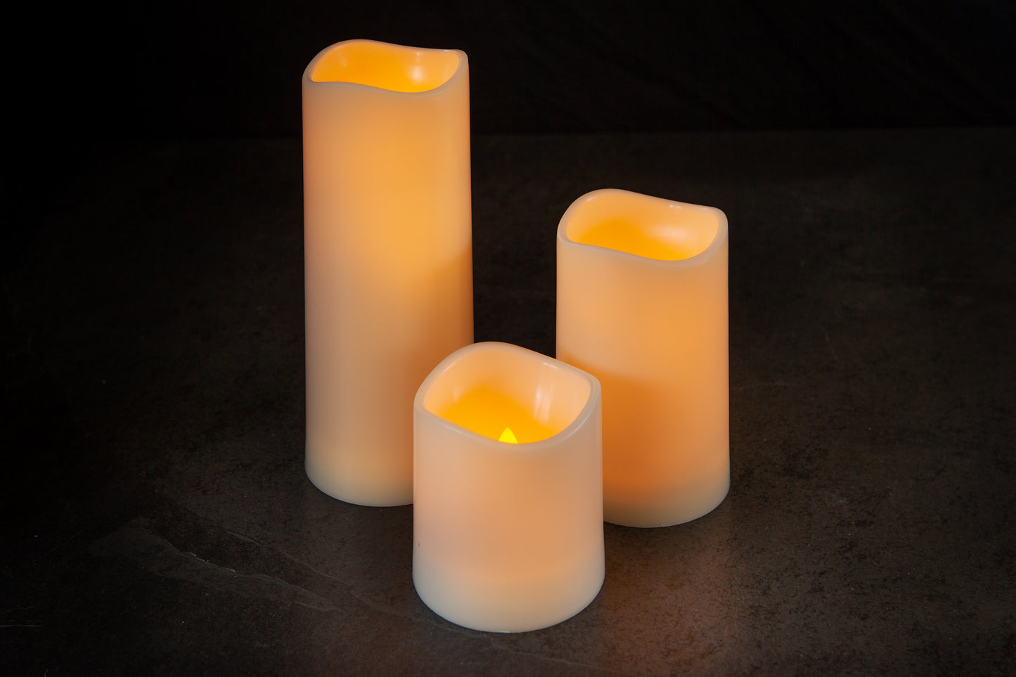 Three illuminated LED candles on a dark surface