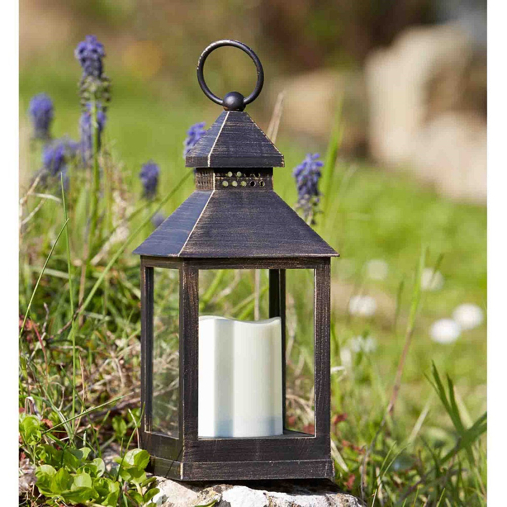 Decorative lantern with a candle in a natural setting with grass and flowers.