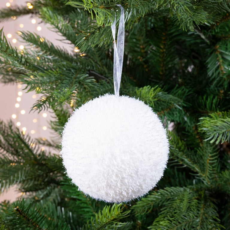 White pom-pom ornament hanging on a Christmas tree with blurred lights in the background