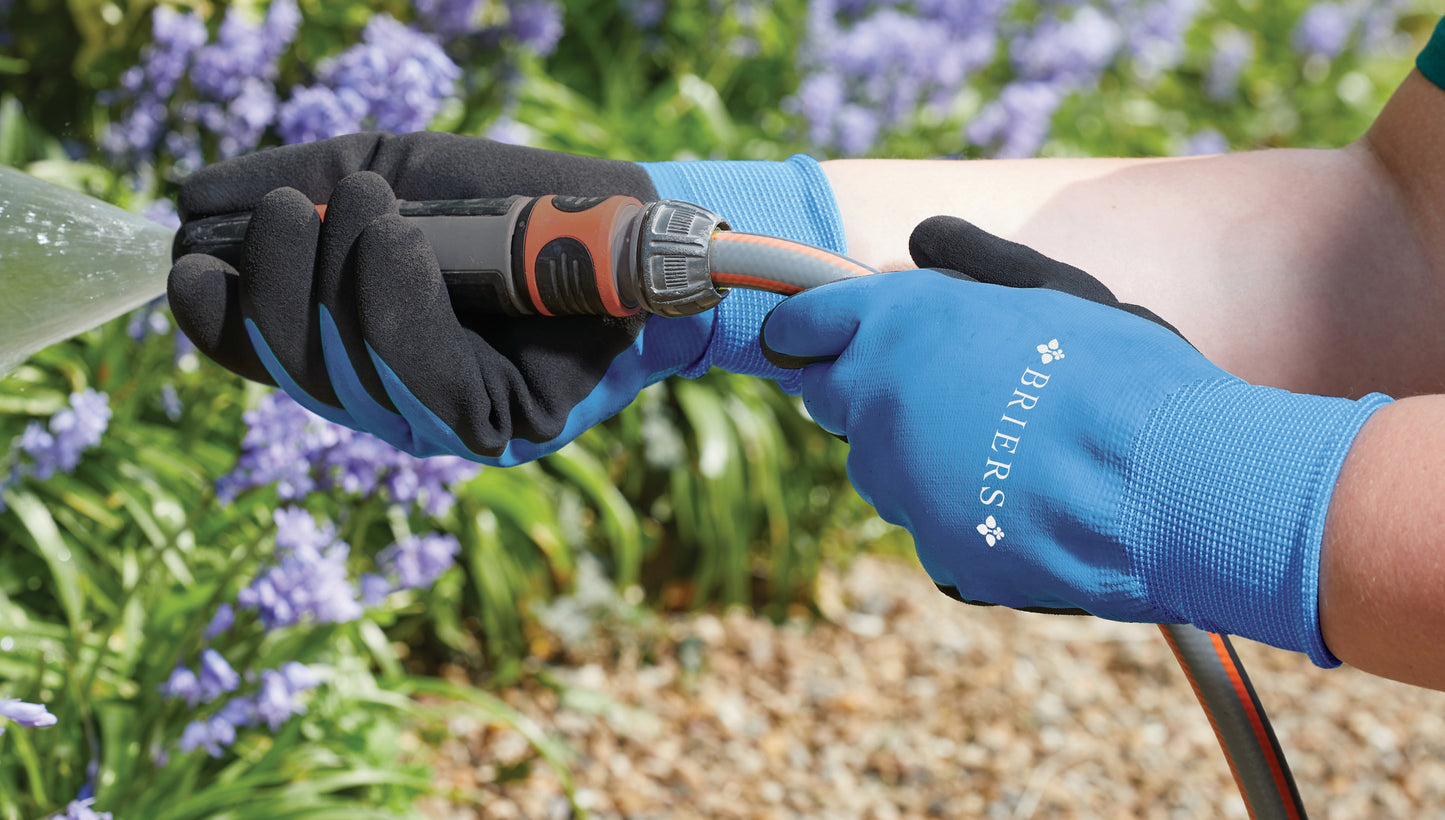 Person wearing blue gloves with 'Biebers' branding, holding a garden tool in a garden setting.