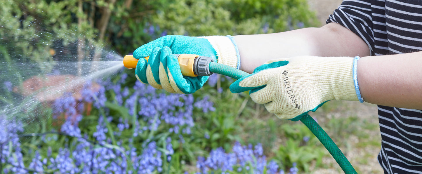 Person watering plants with a garden hose in a garden setting