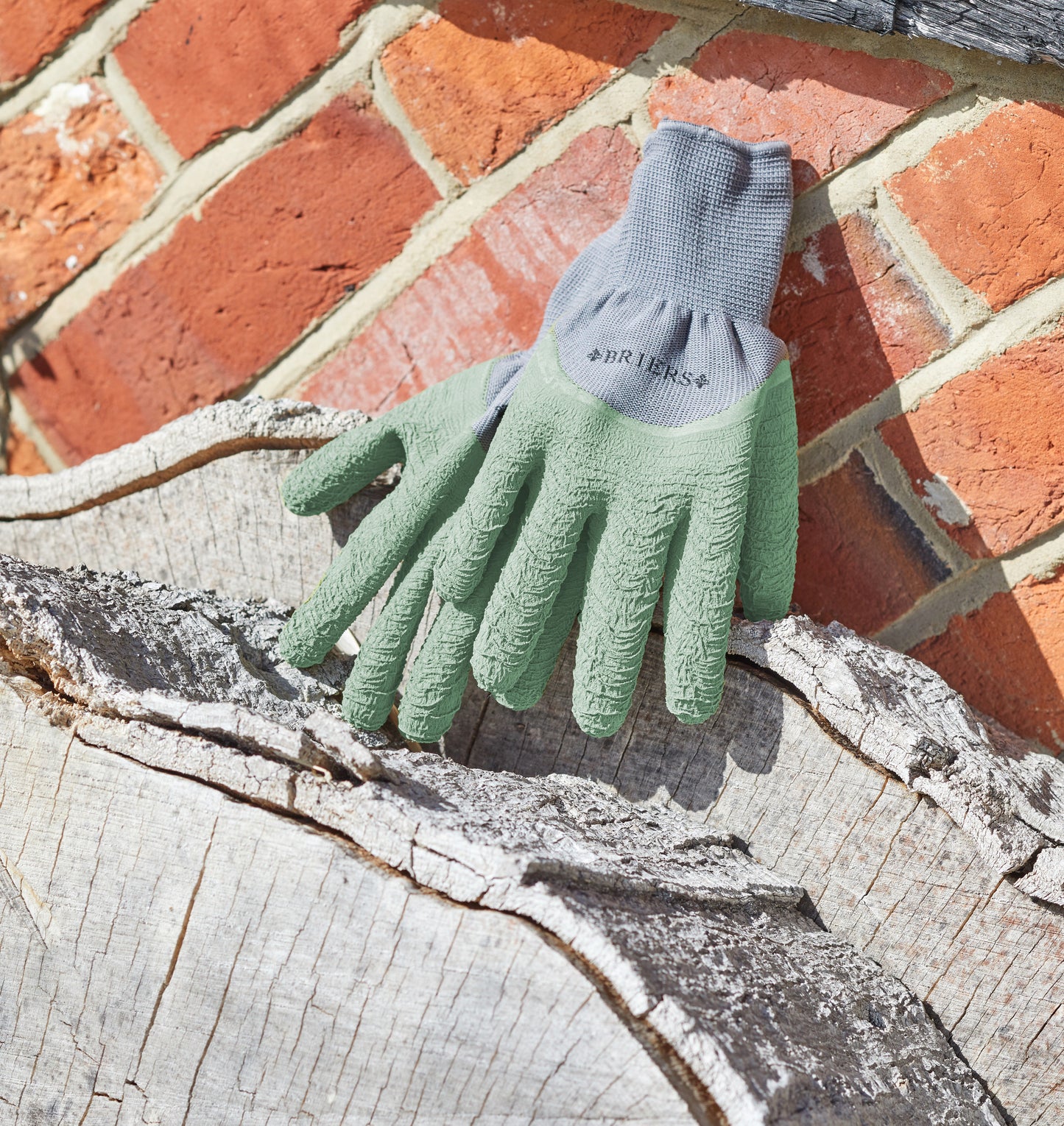 Pair of green gardening gloves on a wooden log with a brick wall background