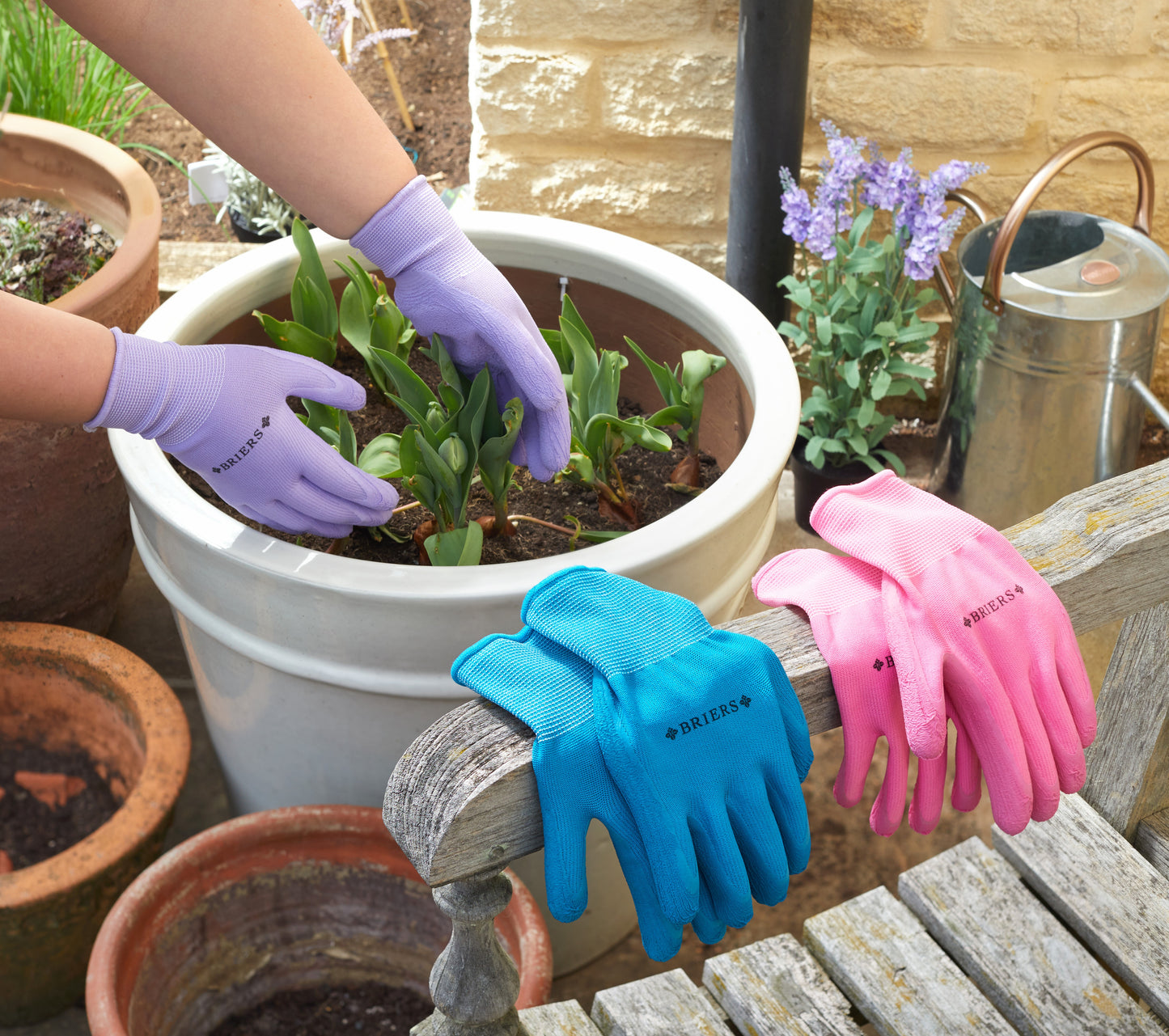Gardening gloves in blue and pink on a wooden table with potted plants in the background.