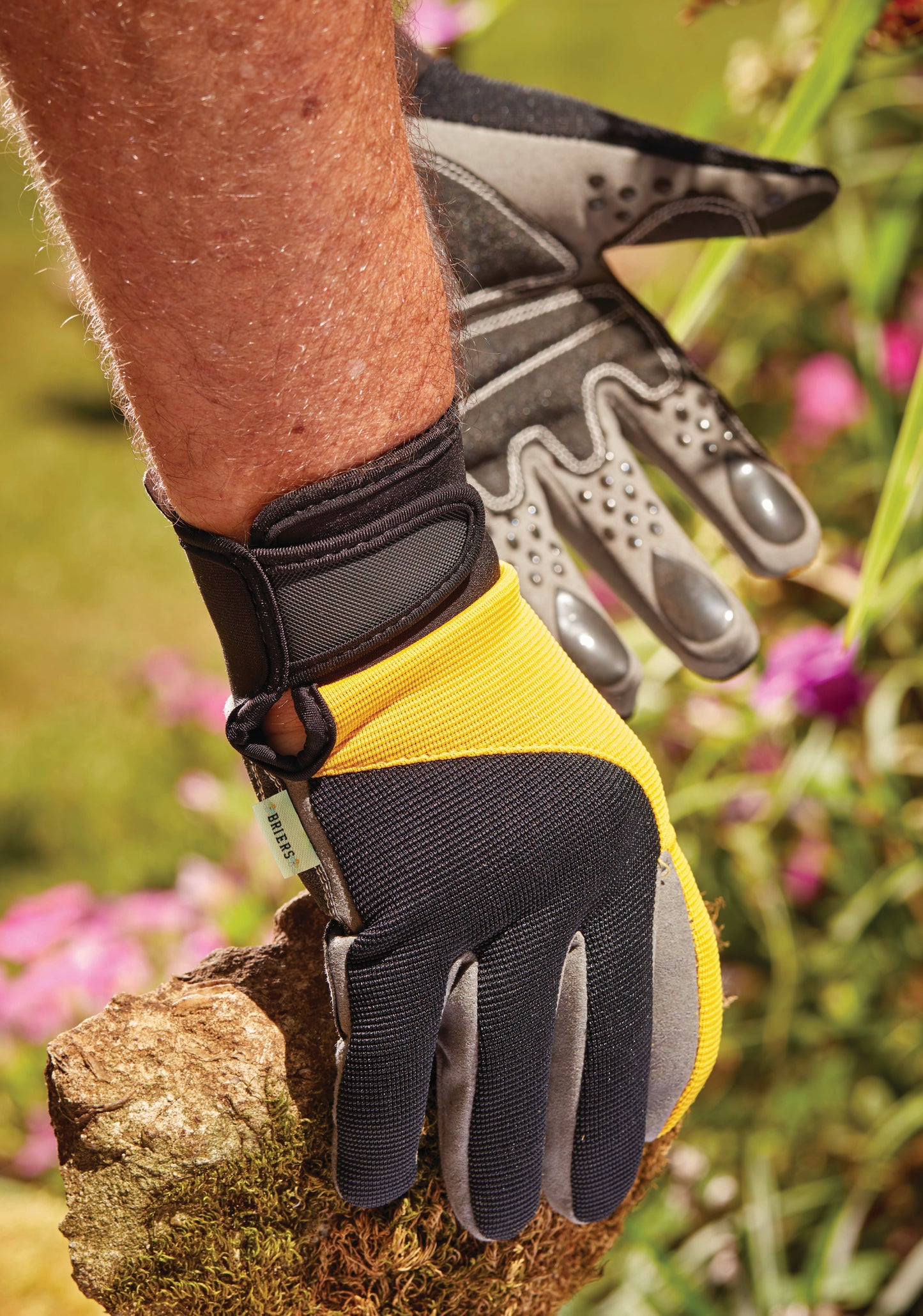 Person wearing a yellow and black gardening glove holding a rock with a blurred natural background