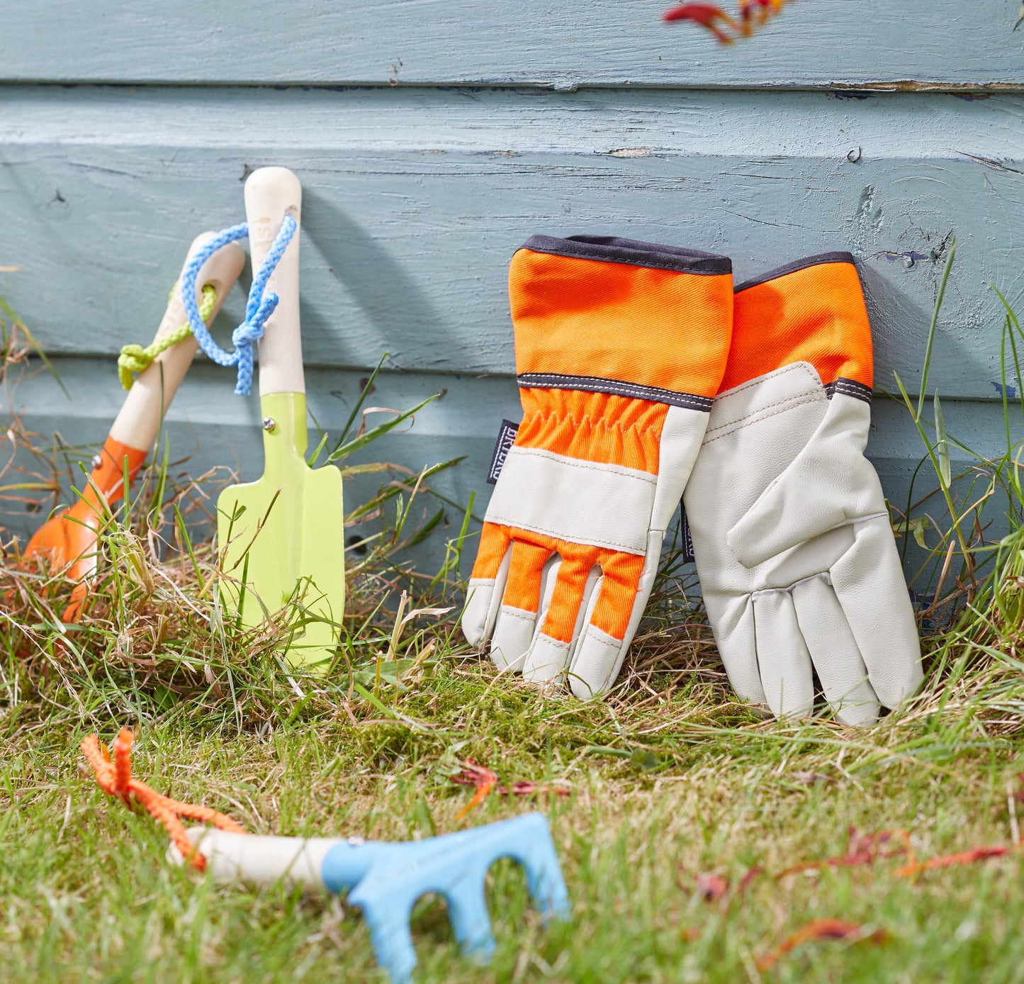 Gardening tools and gloves on grass against a wooden fence