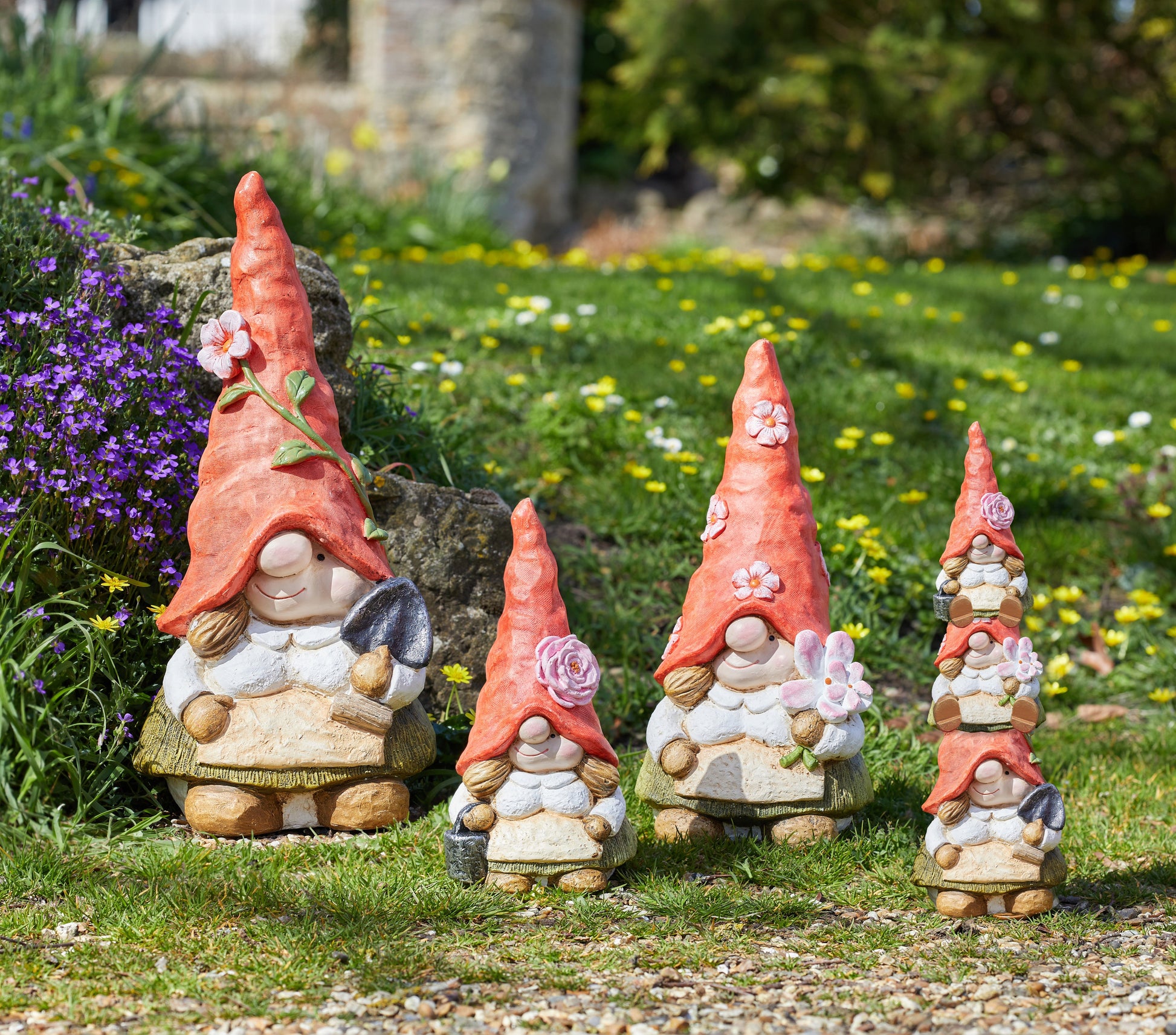 Set of four garden gnomes with red hats and white clothing in a garden setting.
