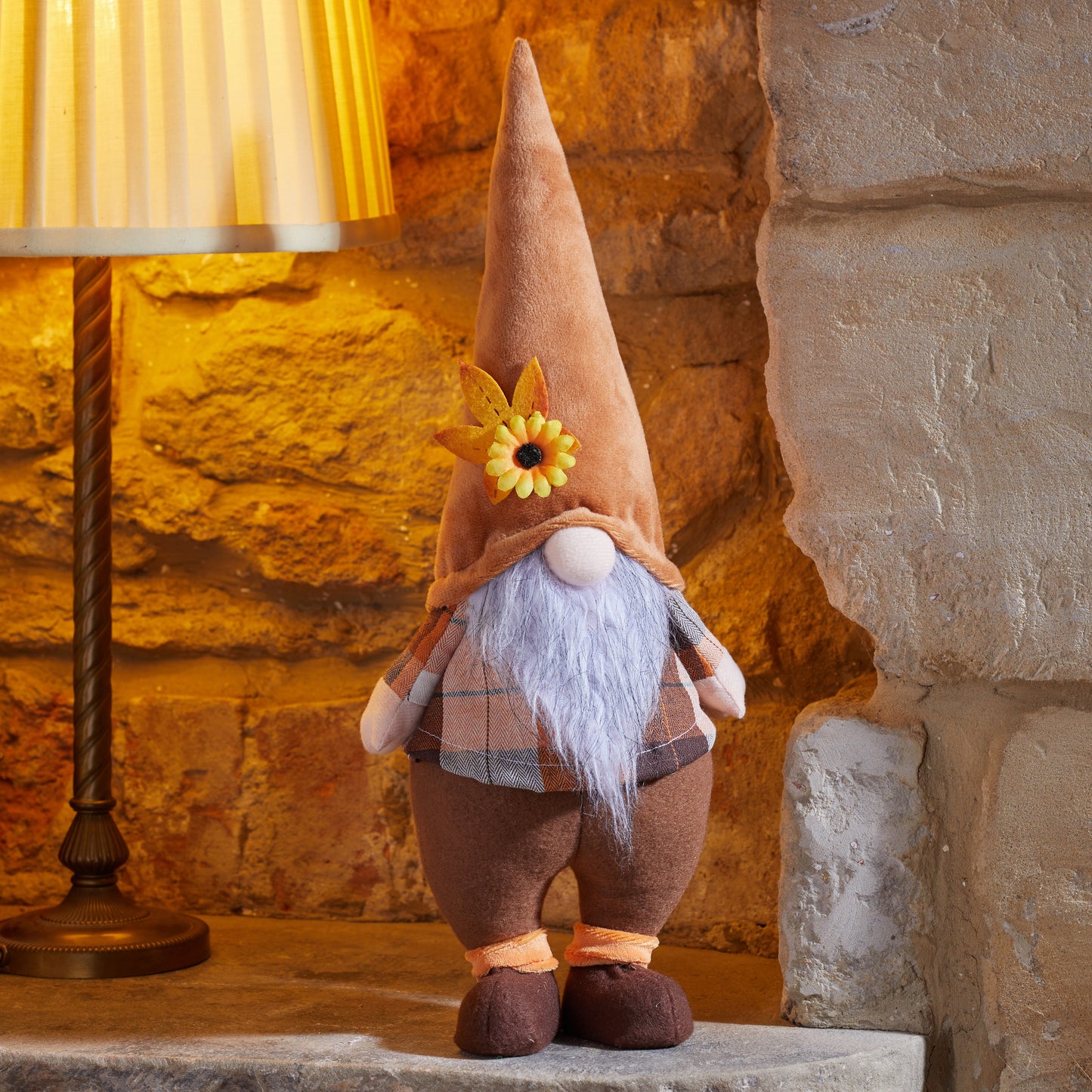 Decorative gnome with a sunflower hat standing on a stone surface next to a lamp.