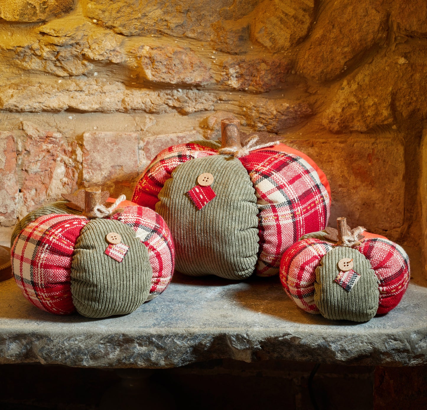Decorative pumpkins made of plaid fabric and corduroy on a stone surface with a stone wall background.
