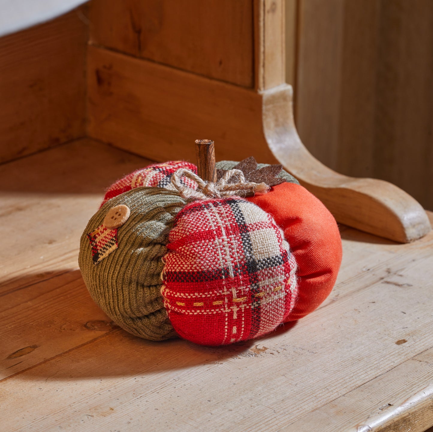 Three fabric pumpkins in plaid and solid colors on a wooden surface.