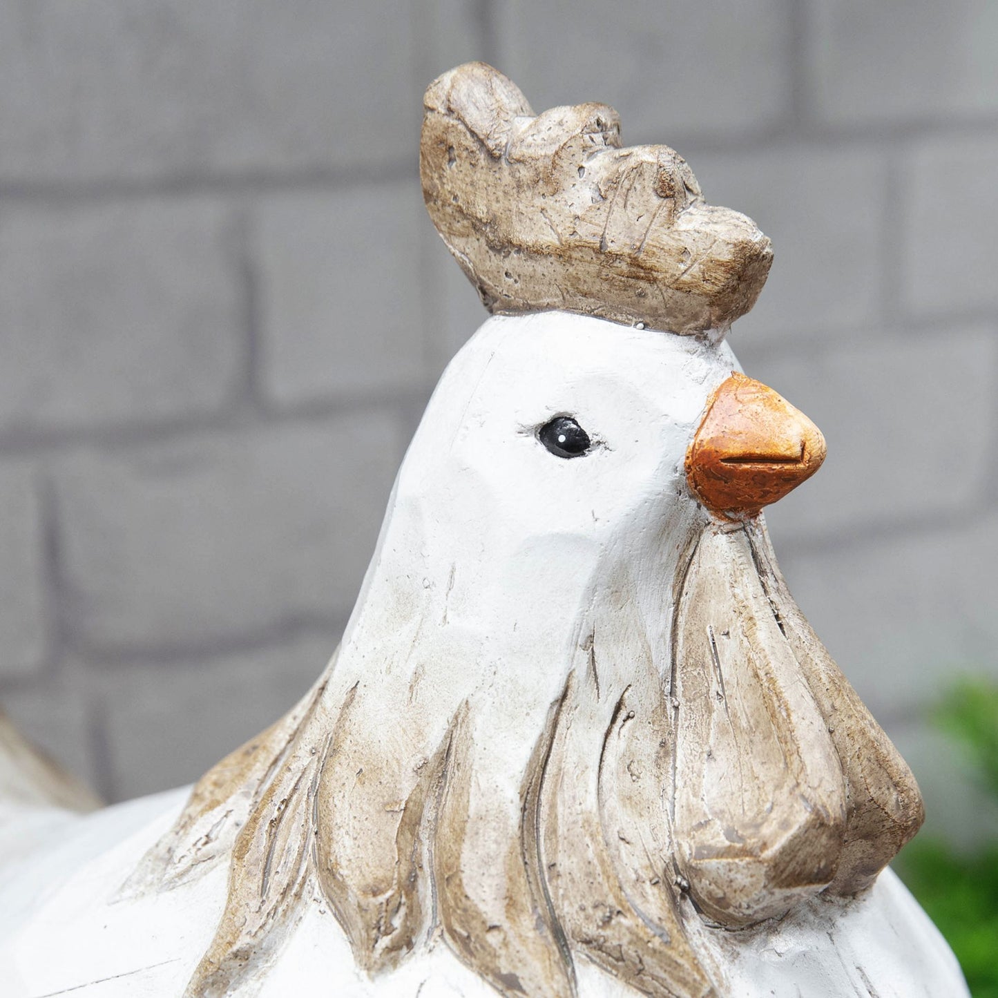 Decorative chicken statue with a crown against a gray brick wall.