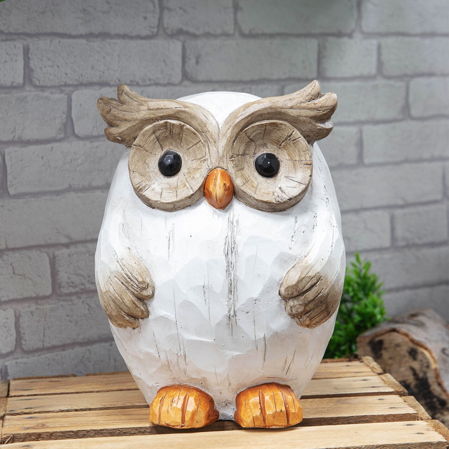 Decorative owl figurine on a wooden surface with a brick wall background