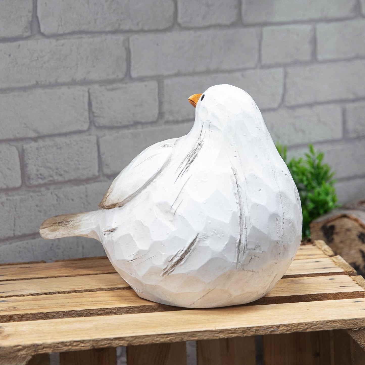 White ceramic dove sculpture on a wooden surface with a brick wall background