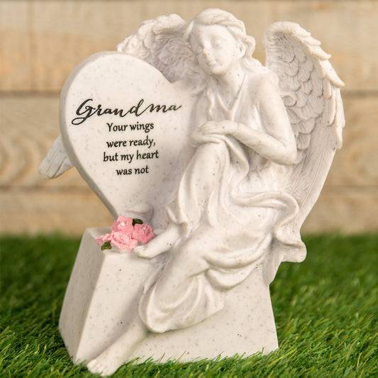 Statue of an angel holding a heart with text and flowers on grass