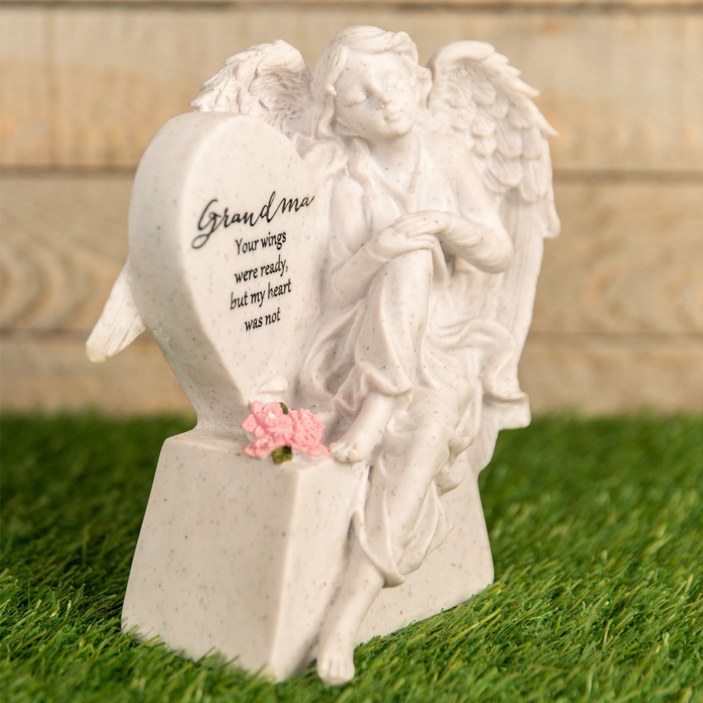 White angel statue with text and pink flower on a grassy background