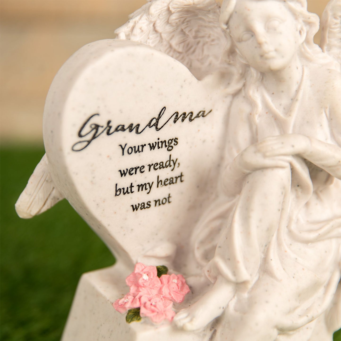 Statue of an angel with a heart-shaped plaque and pink flowers, featuring text.
