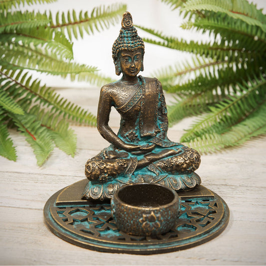 Bronze Buddha statue with a small bowl on a wooden surface with ferns in the background
