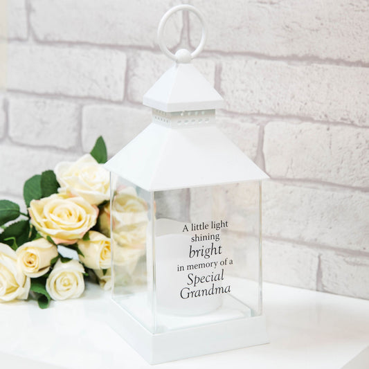 White lantern with engraved text next to white roses on a light background