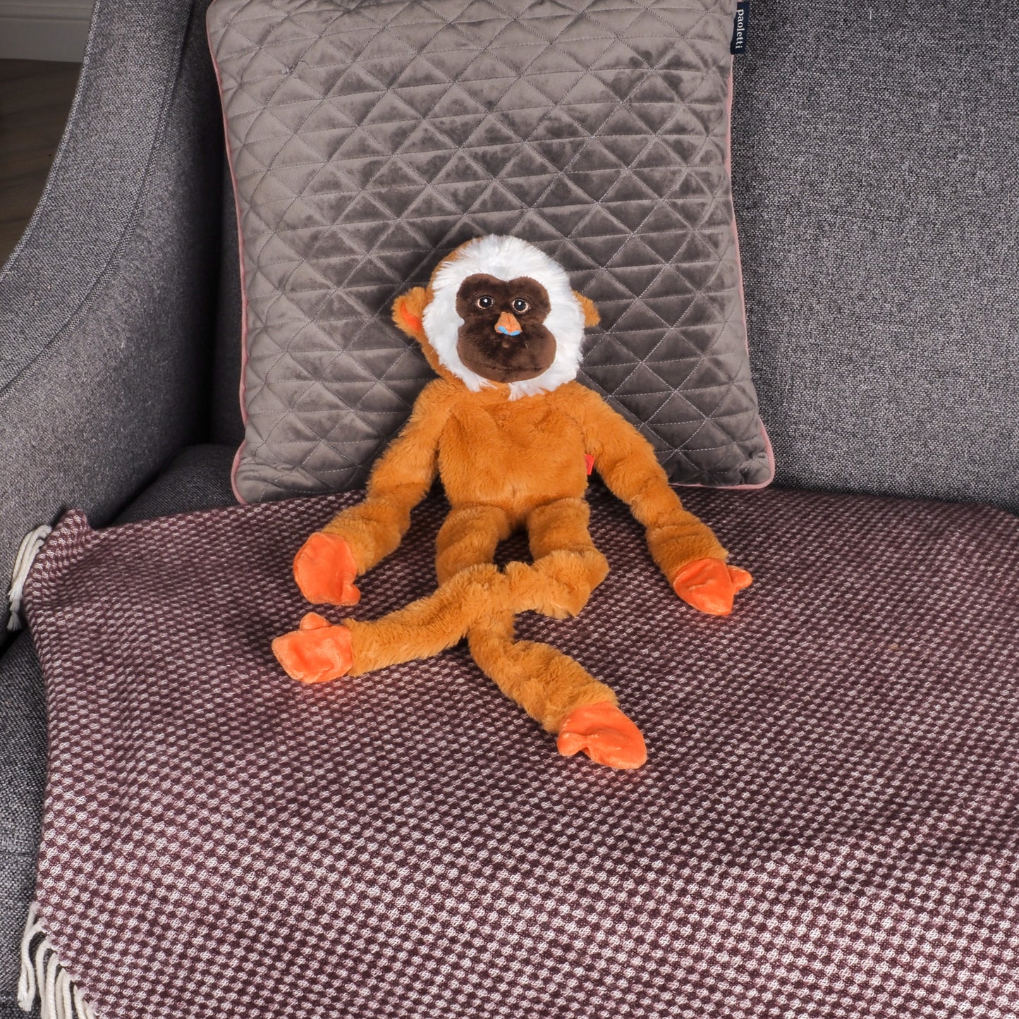 Plush monkey toy on a textured surface with pillows in the background