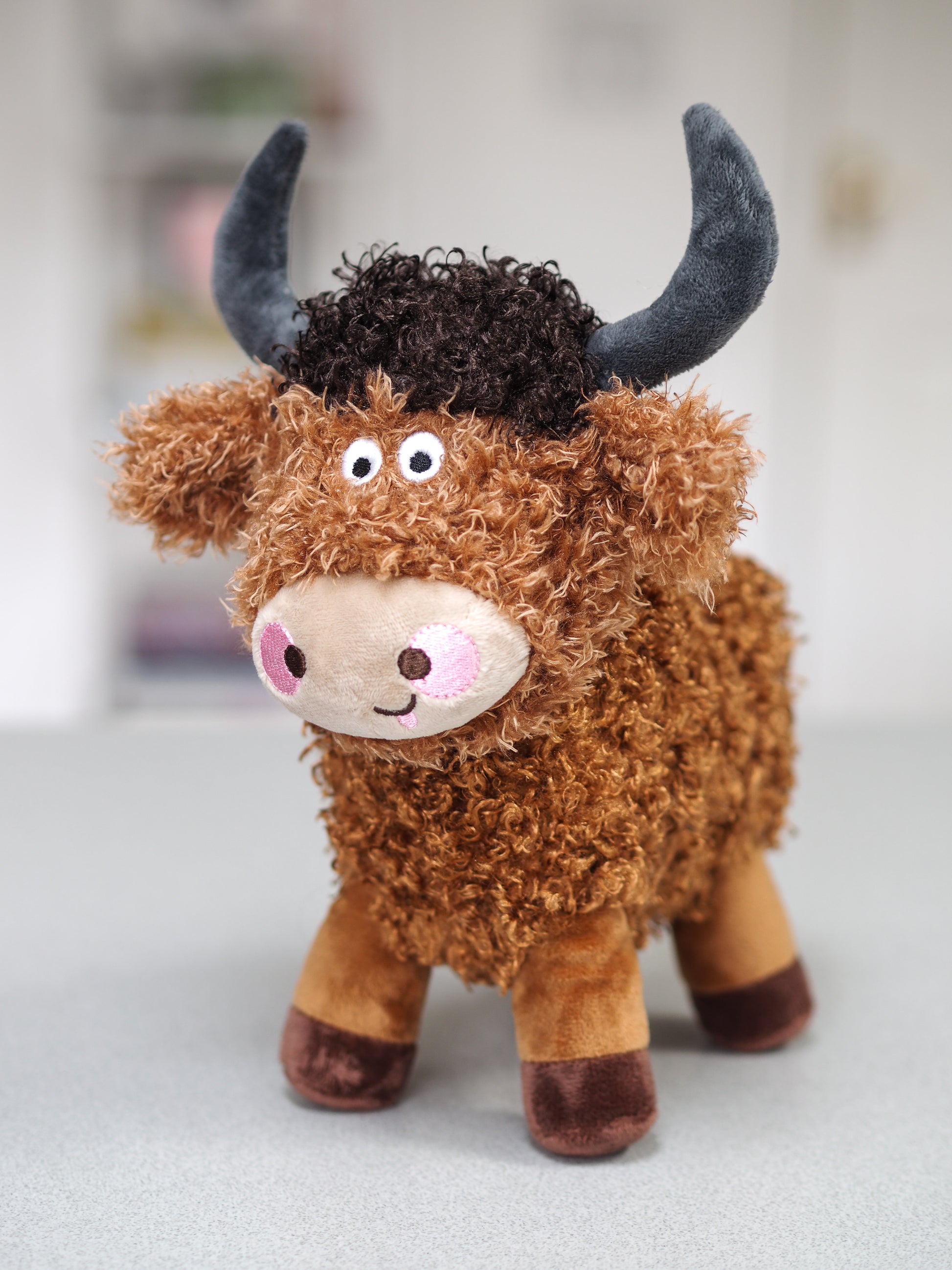 Plush toy yak with brown fur and black horns on a light gray background