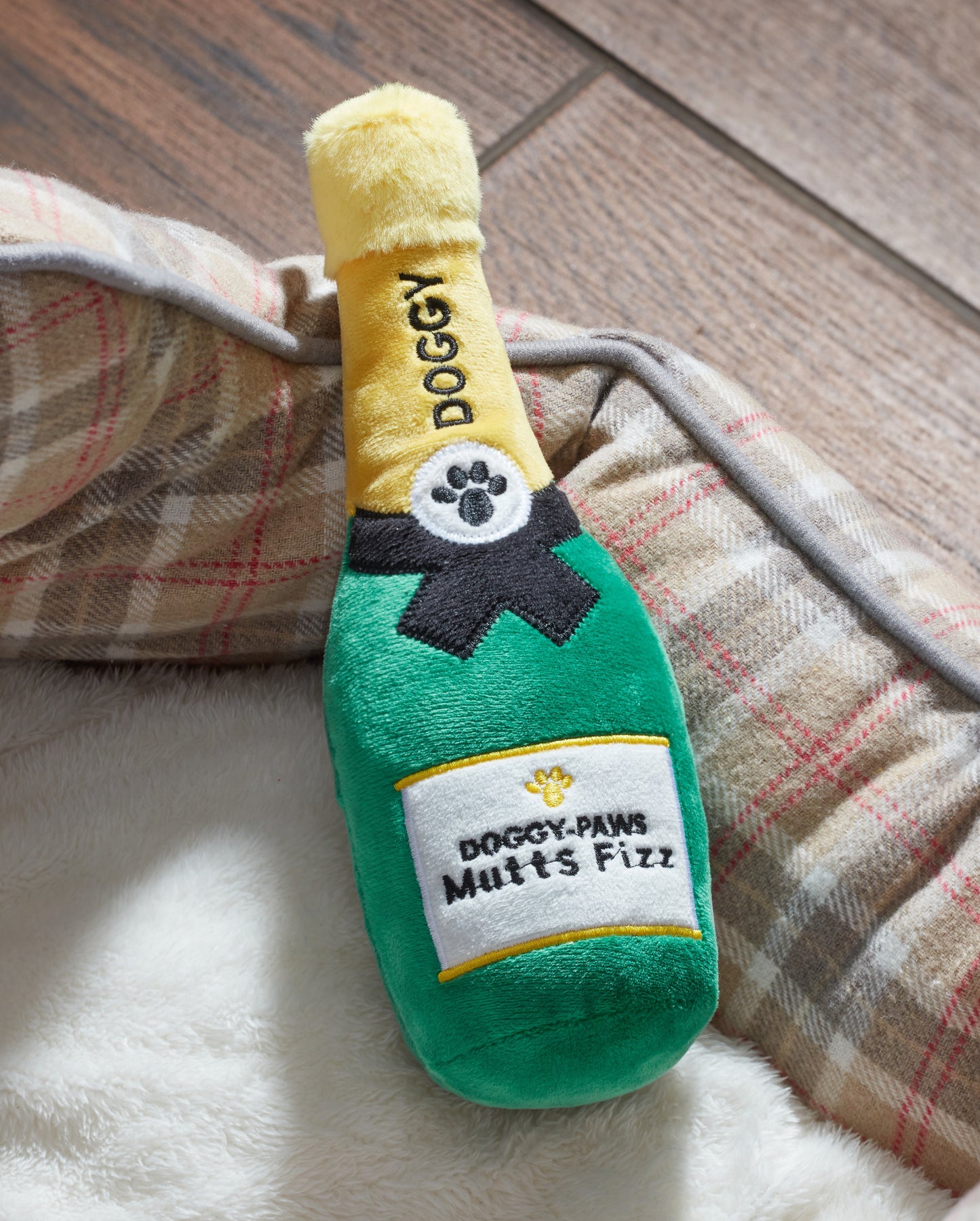 Dog toy shaped like a champagne bottle with 'Doggy' branding on a wooden floor.