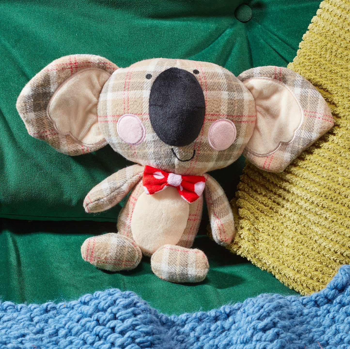 Plush koala toy with a red bow tie on a green fabric background