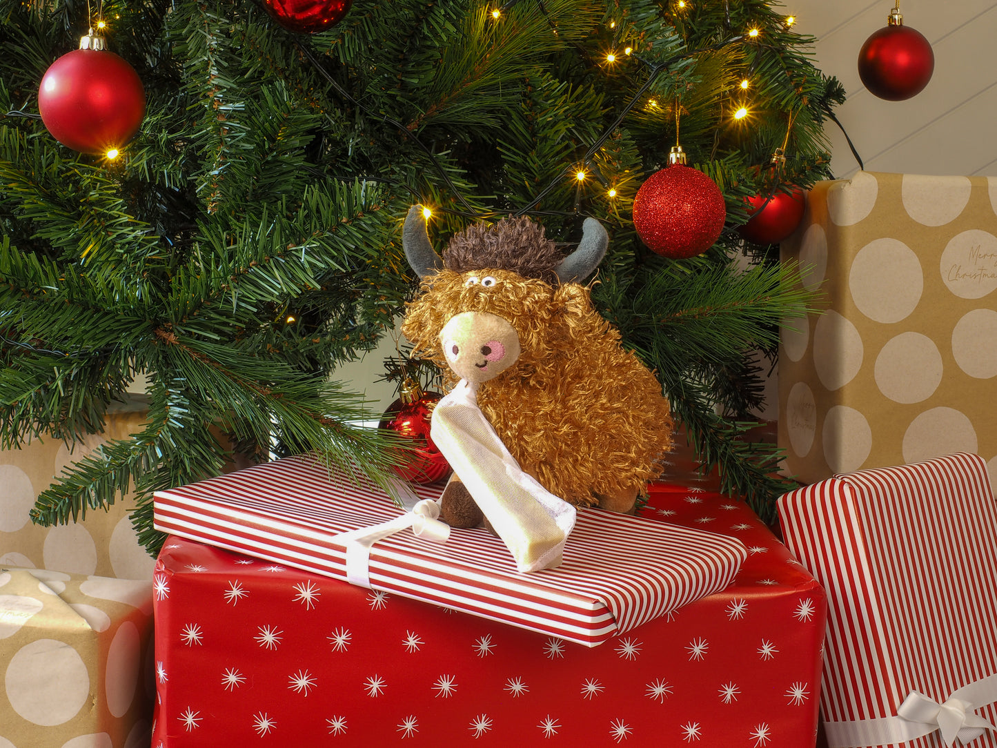 Stuffed animal toy on a red gift box under a decorated Christmas tree with presents.