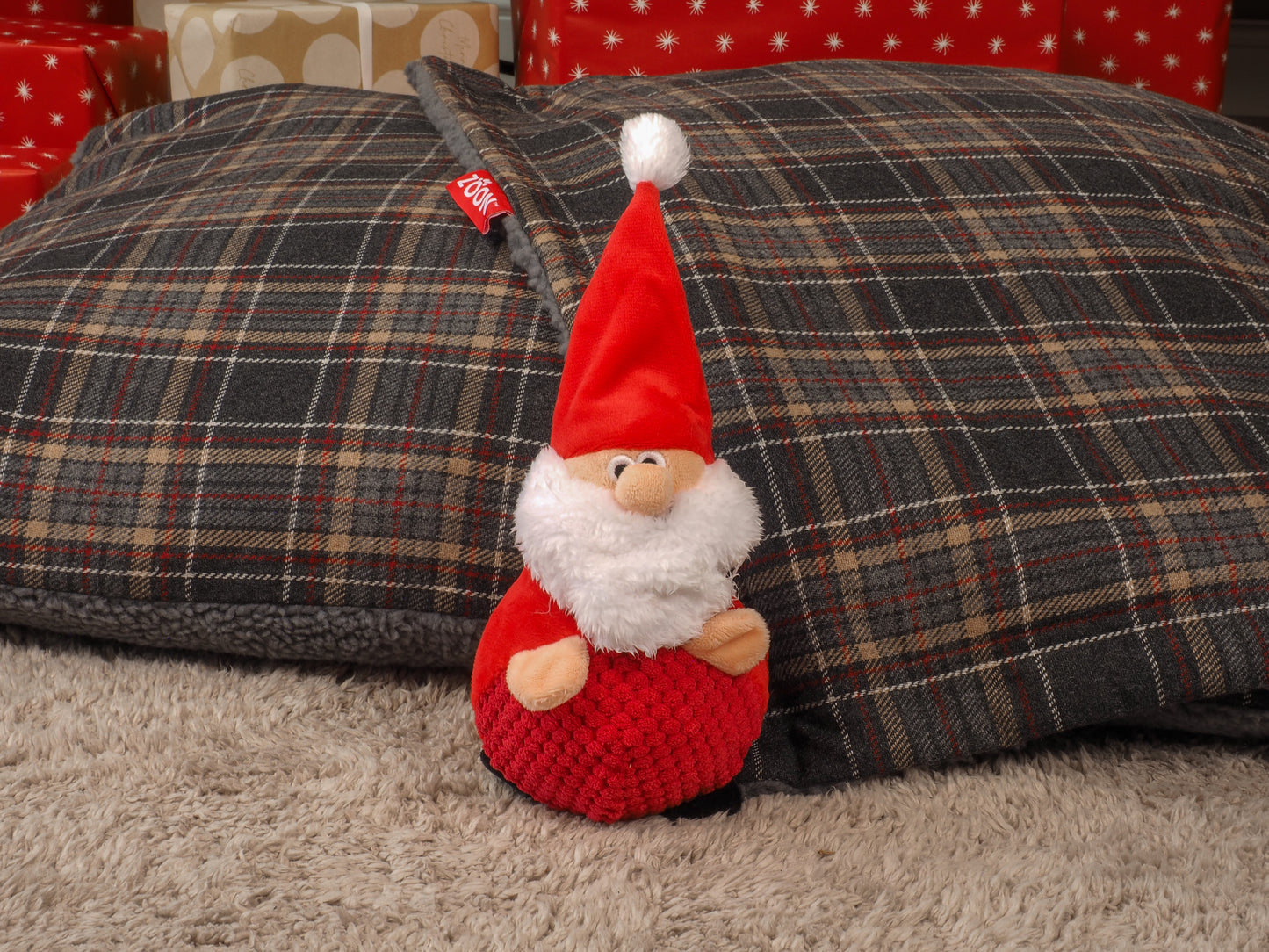 Small gnome figurine with a red hat and outfit on a plaid cushion.