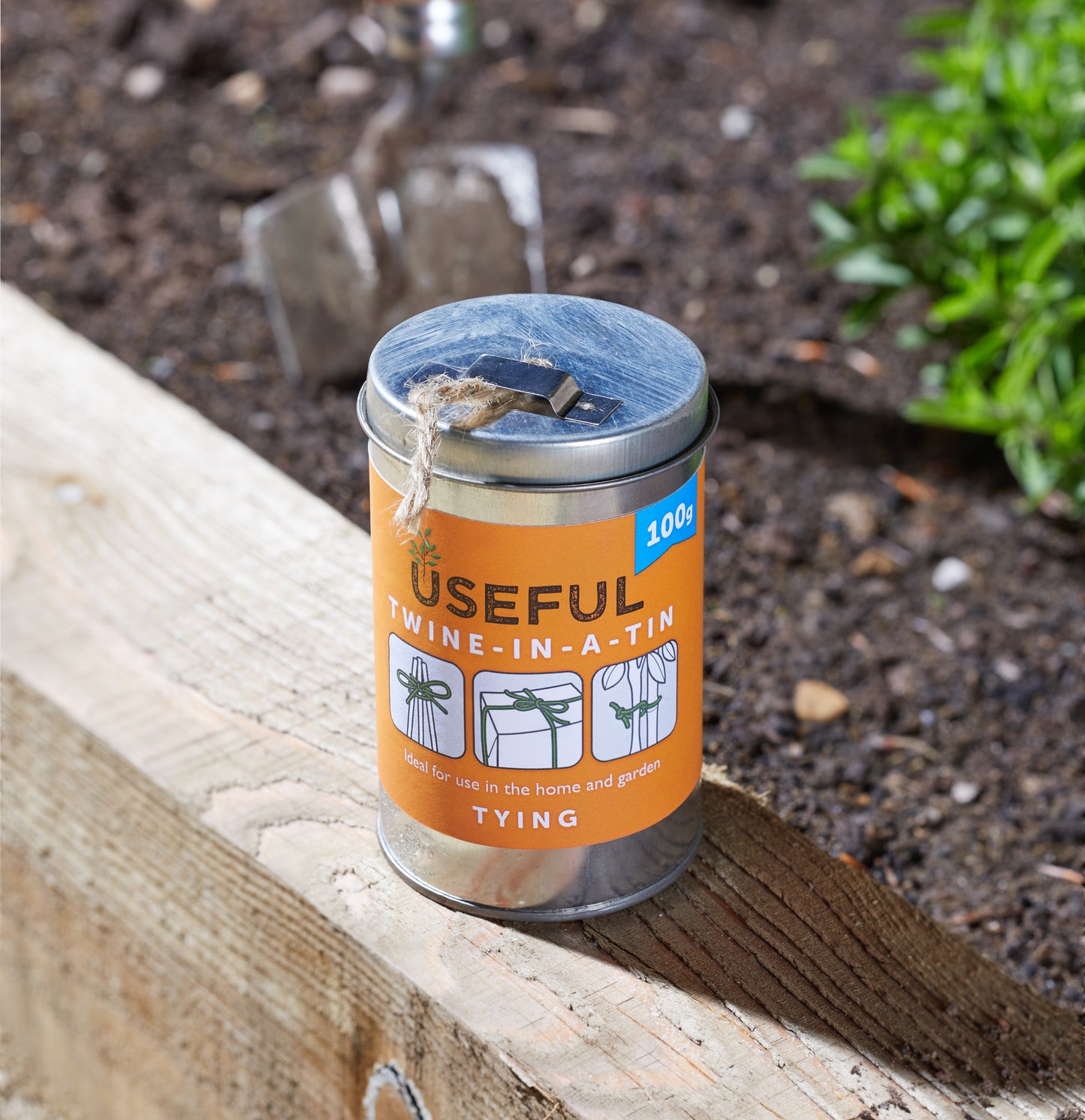 Can of Useful Twine-In-A-Tin on a wooden surface with garden tools in the background