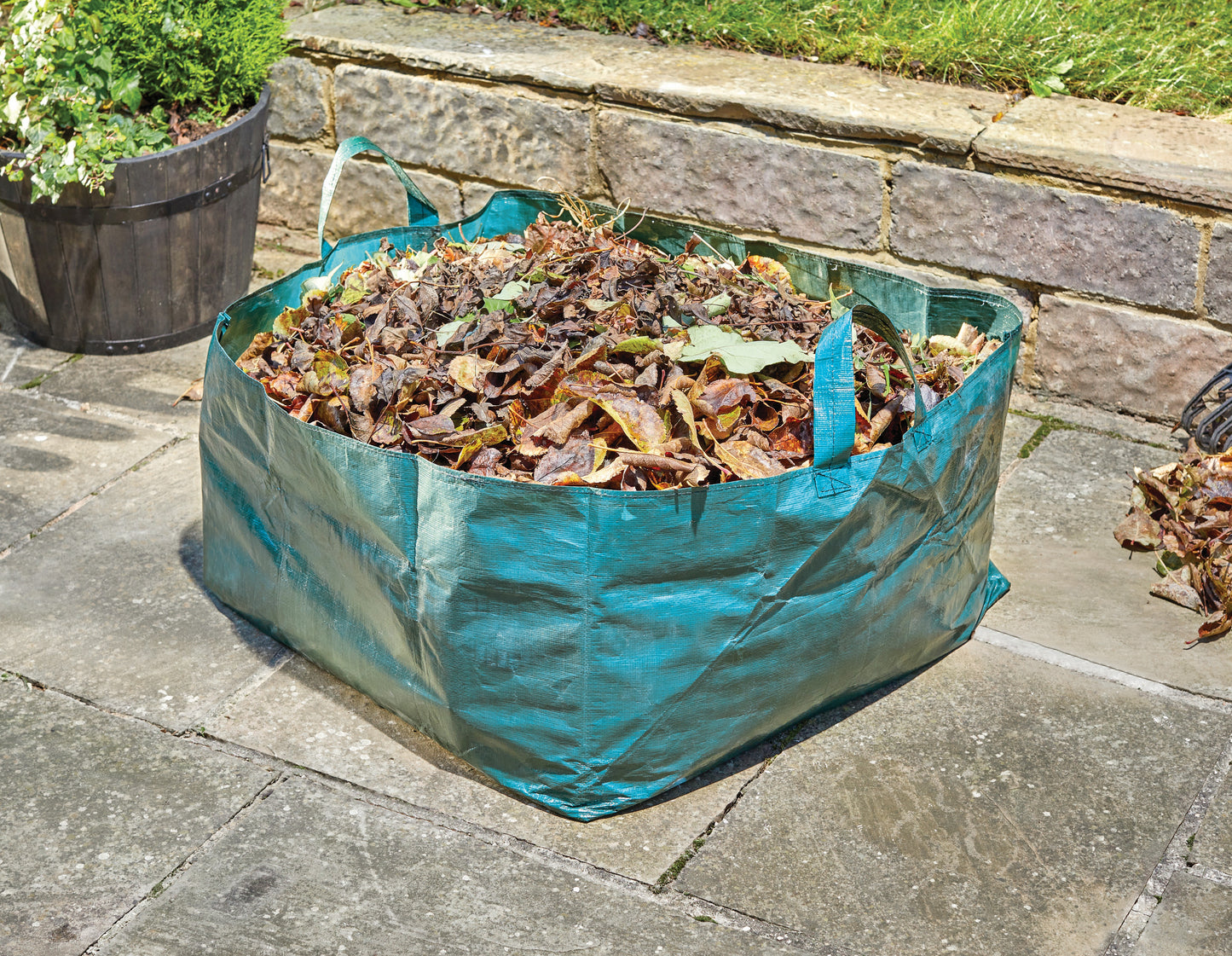 Green garden waste bag filled with leaves on a stone patio