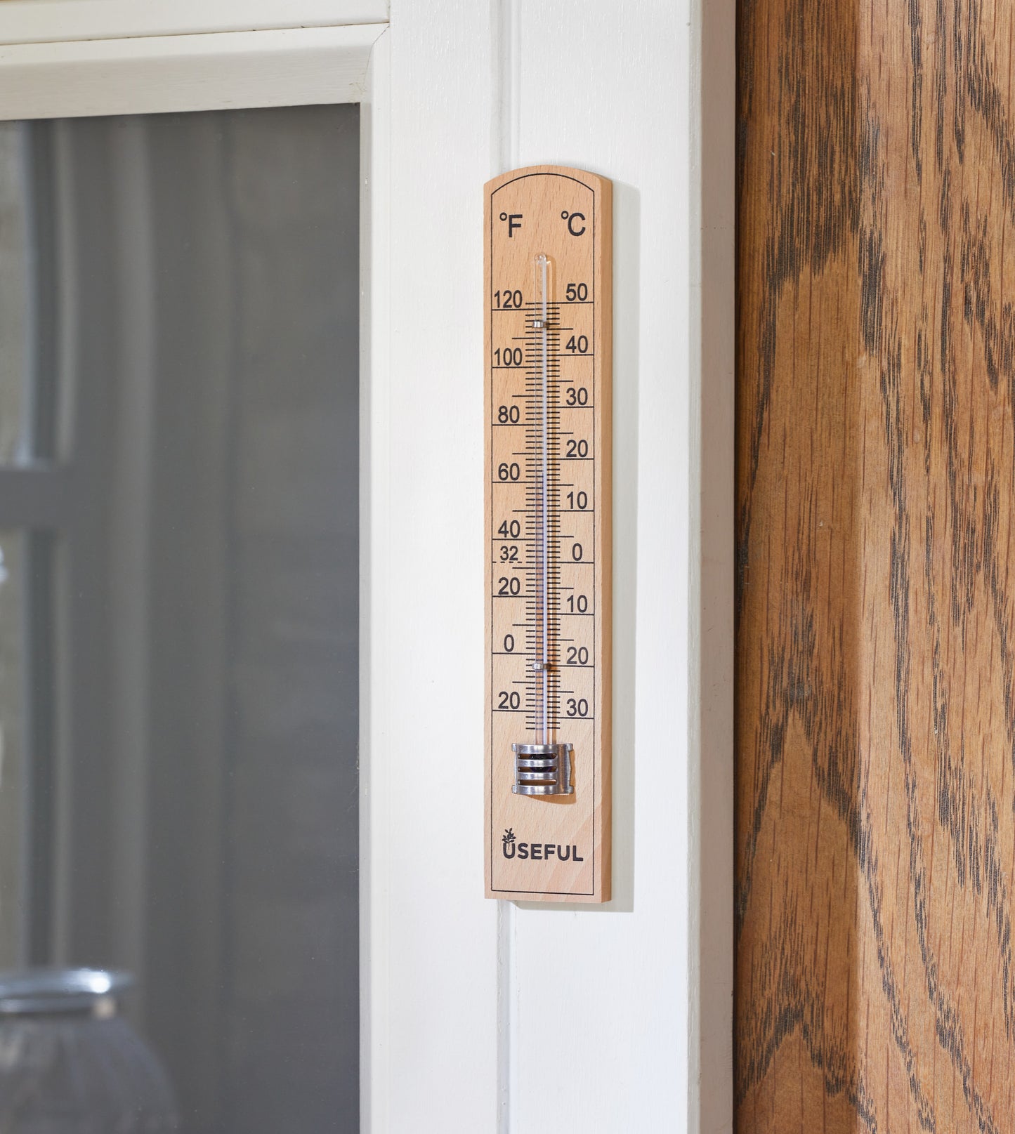 Wooden thermometer attached to a door with a wooden surface and glass panel in the background.