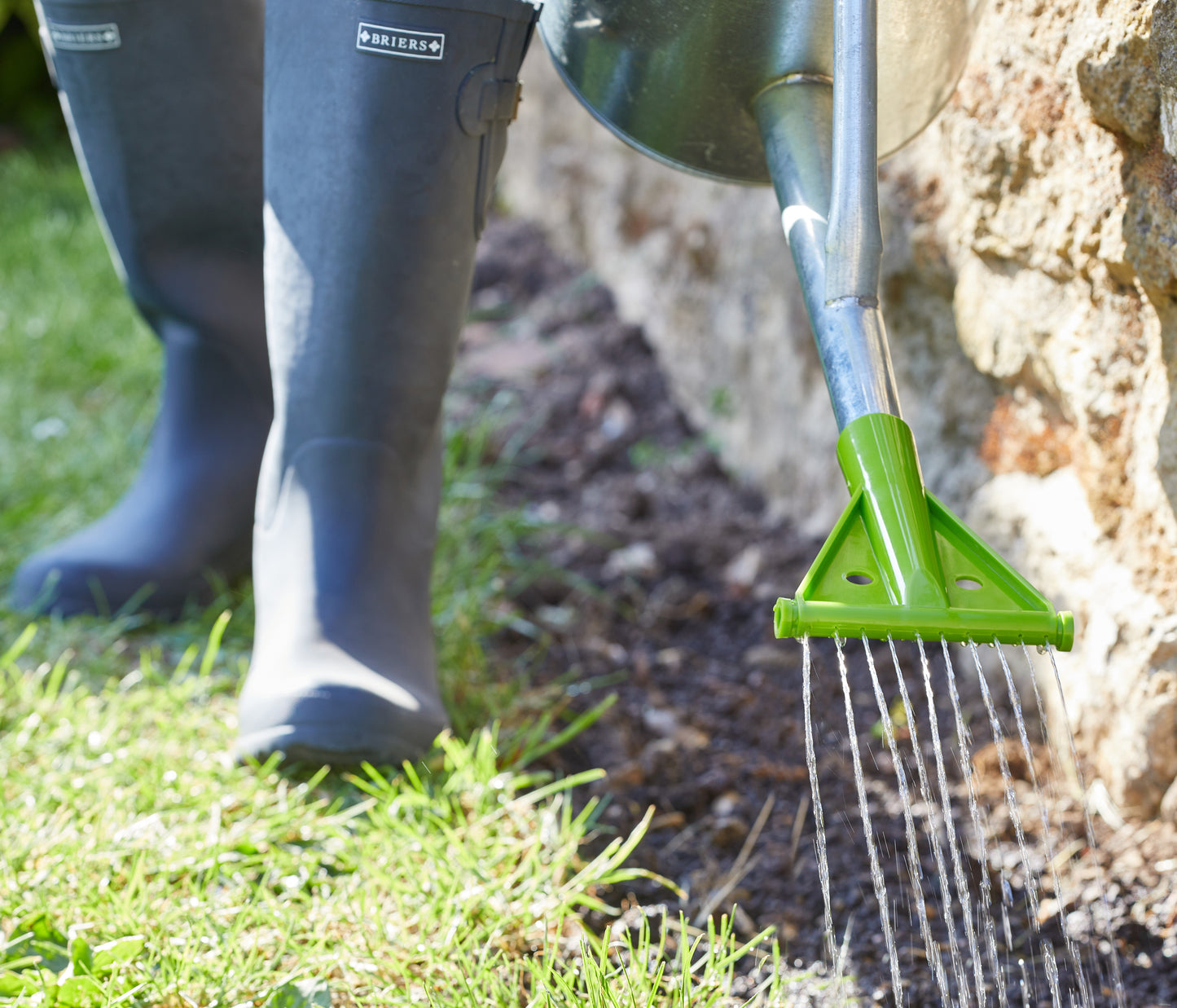 Person using a green garden tool to water a tree in a garden setting