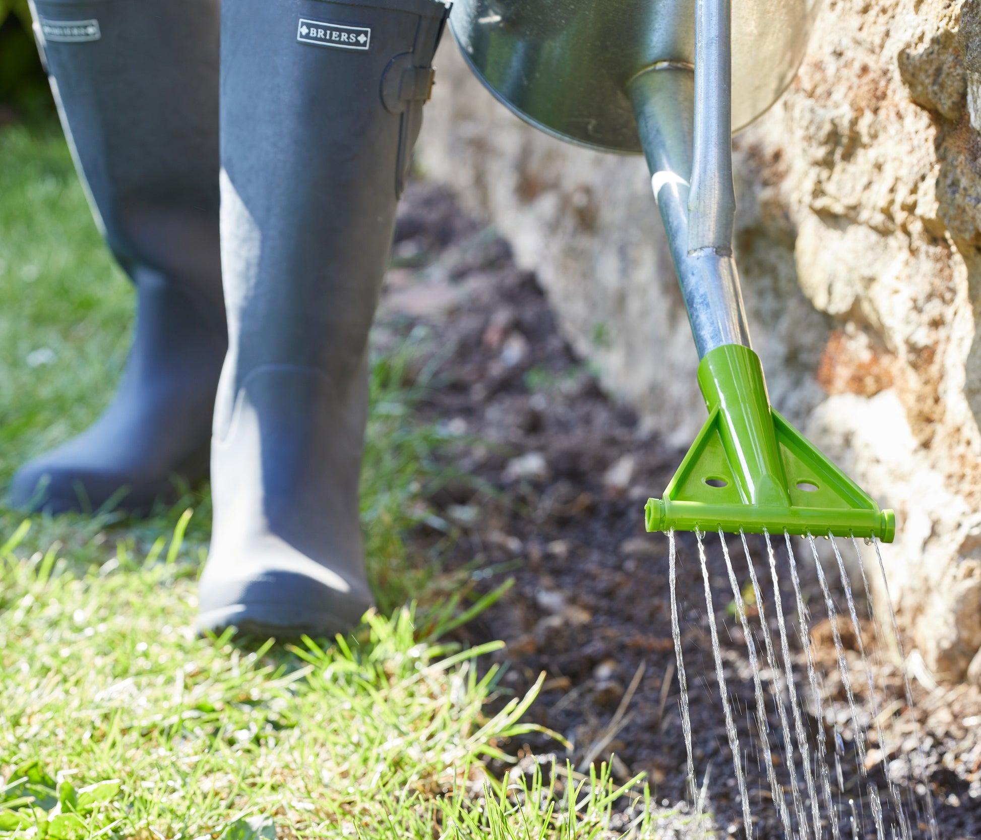 Person using a green garden tool to water a tree in a garden setting