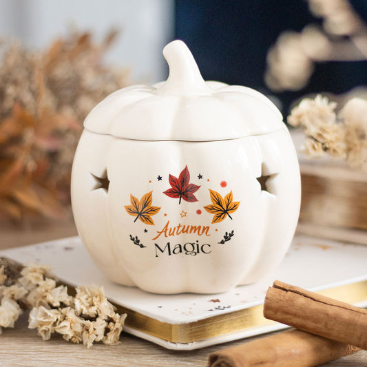 White ceramic pumpkin-shaped container with 'Autumn Magic' text and leaf designs on a wooden surface.