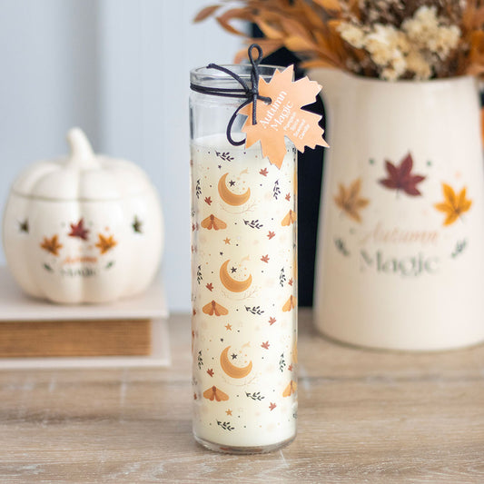 Decorative candle with autumn-themed design on a wooden surface with pumpkins and leaves in the background.
