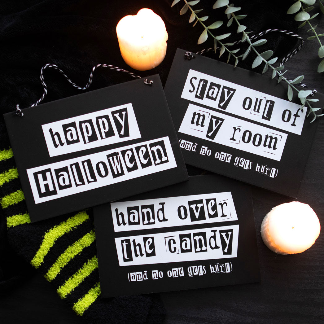 Halloween-themed signs with text on a dark background with candles and greenery.