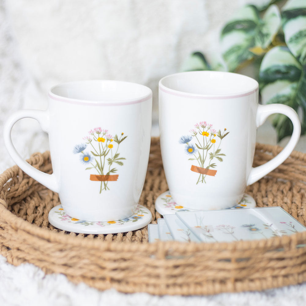 Two white mugs with floral designs on a woven tray with coasters.