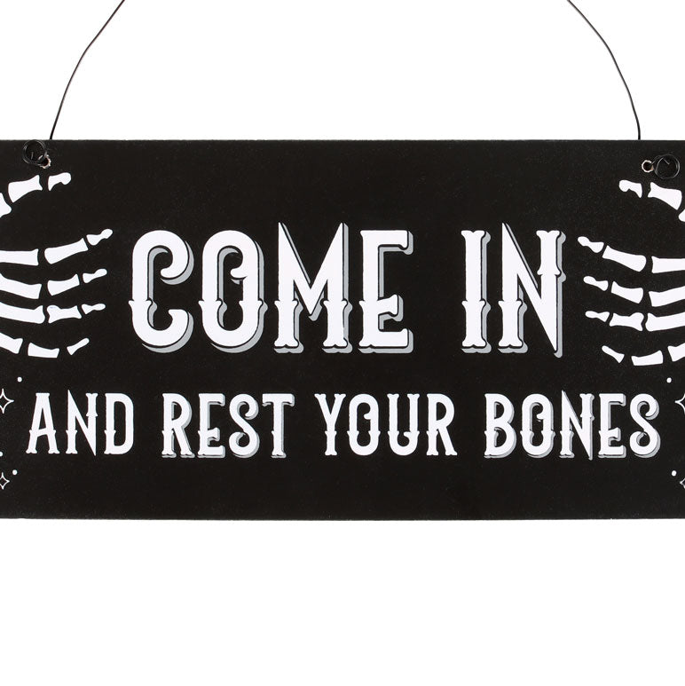 Decorative sign with skeleton hands and text 'COME IN AND REST YOUR BONES' on a black background.