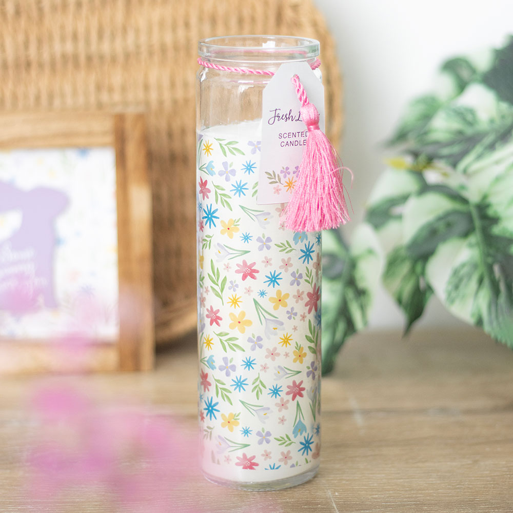 Decorative candle with floral pattern and pink tassel on a wooden surface.