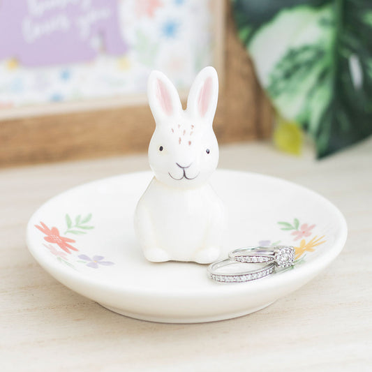 White ceramic rabbit on a decorative plate with floral designs, placed on a light surface.